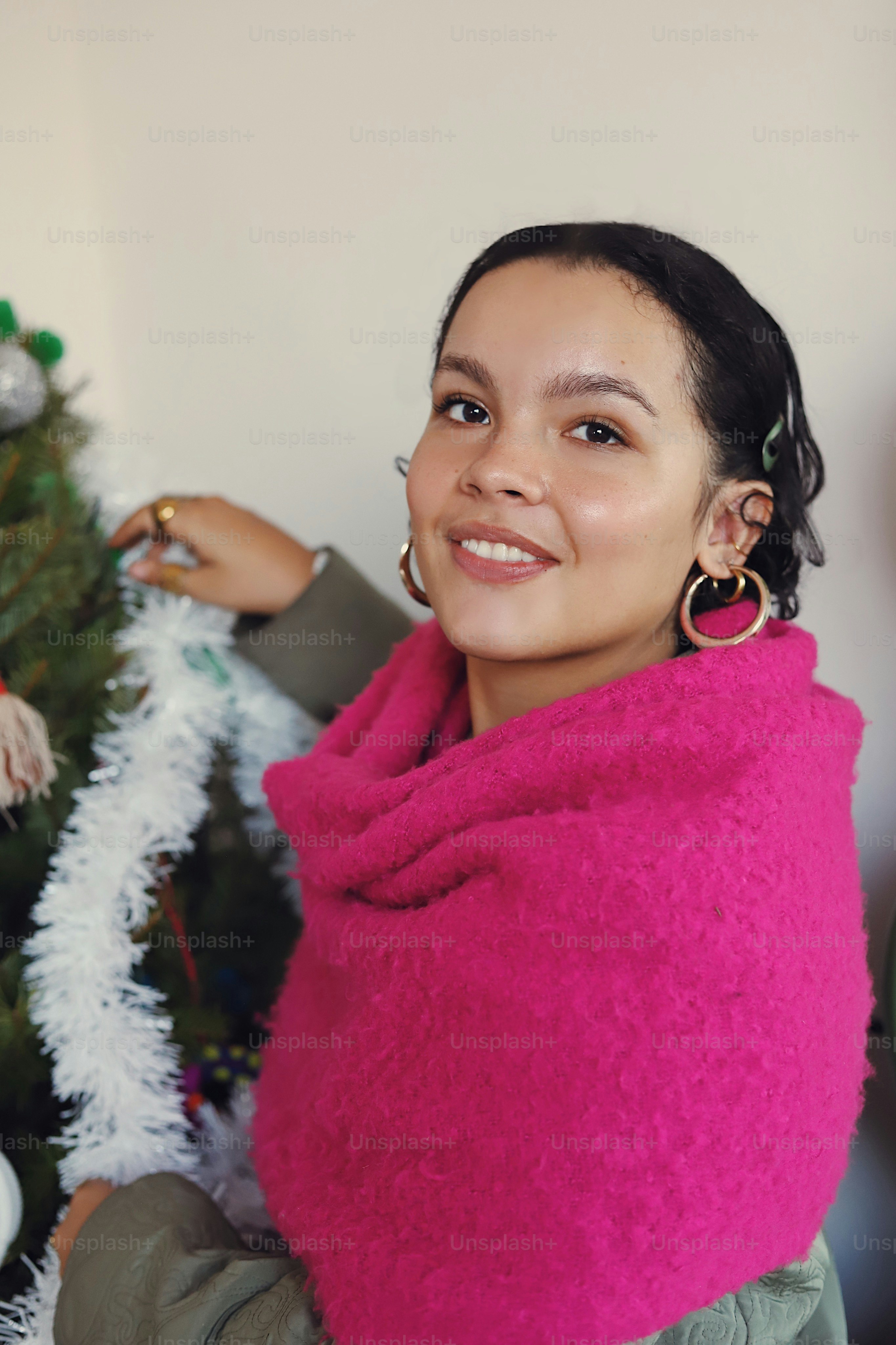 A woman wearing a pink scarf next to a christmas tree