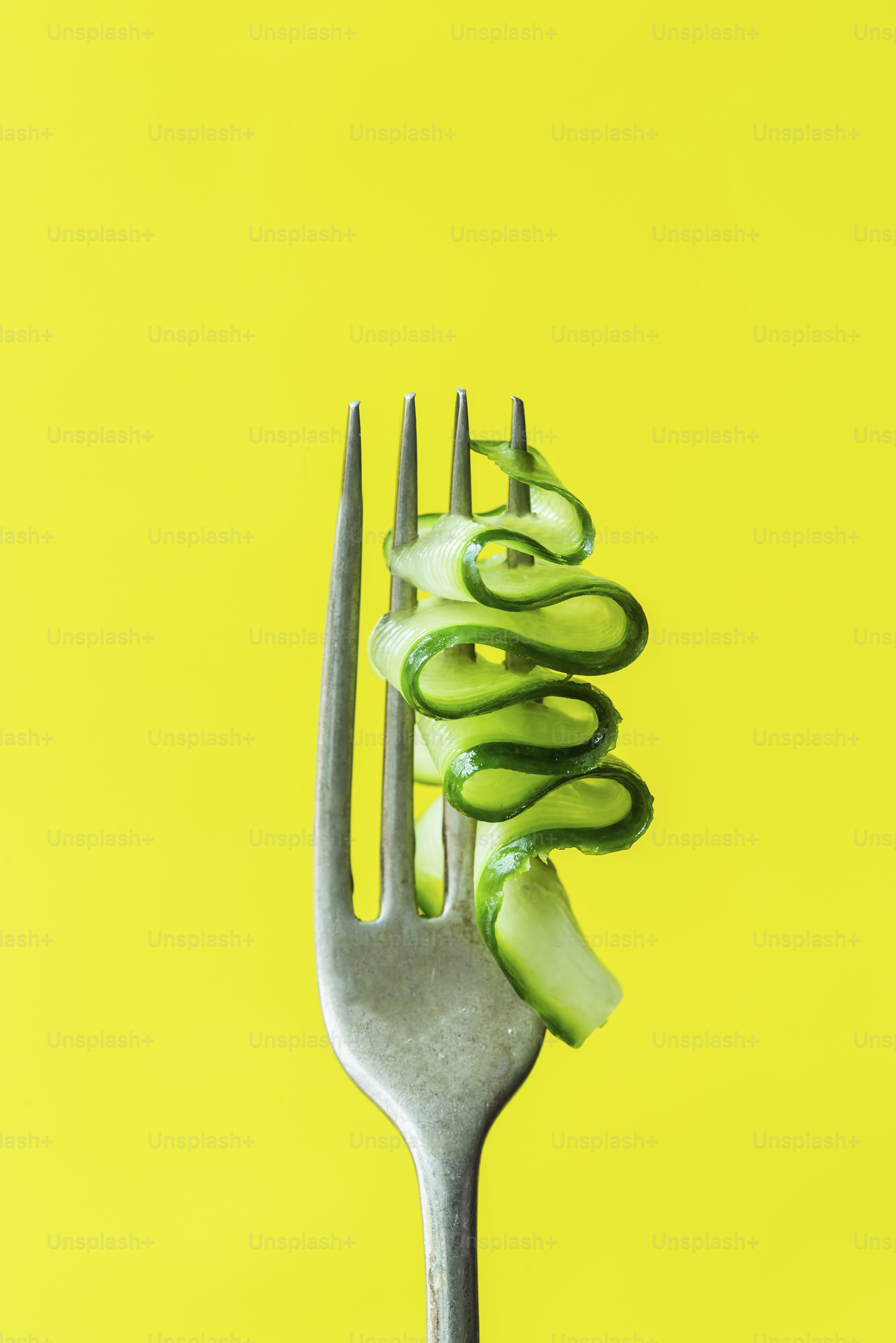 A fork with cucumbers on it on a yellow background