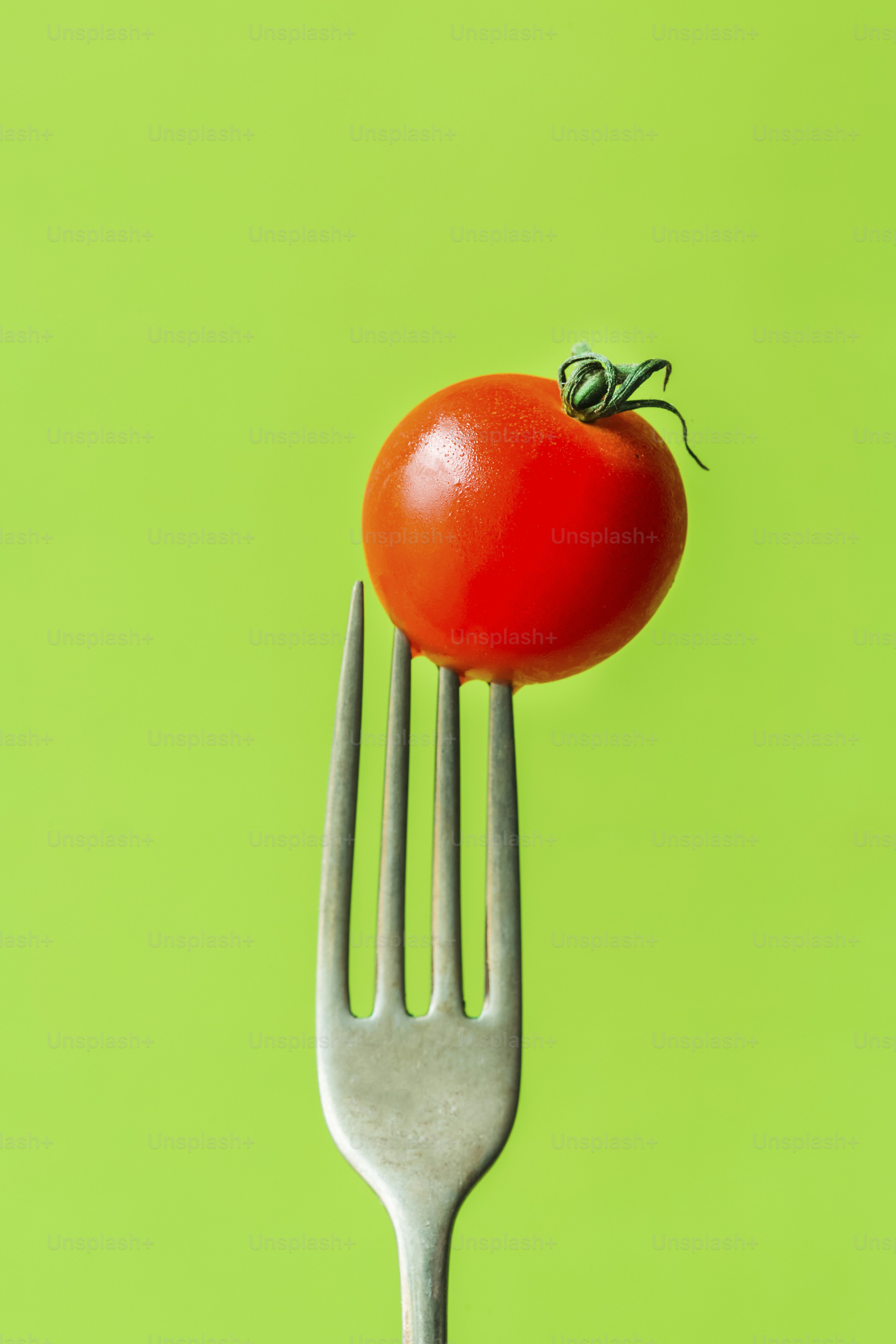 A tomato on a fork on a green background