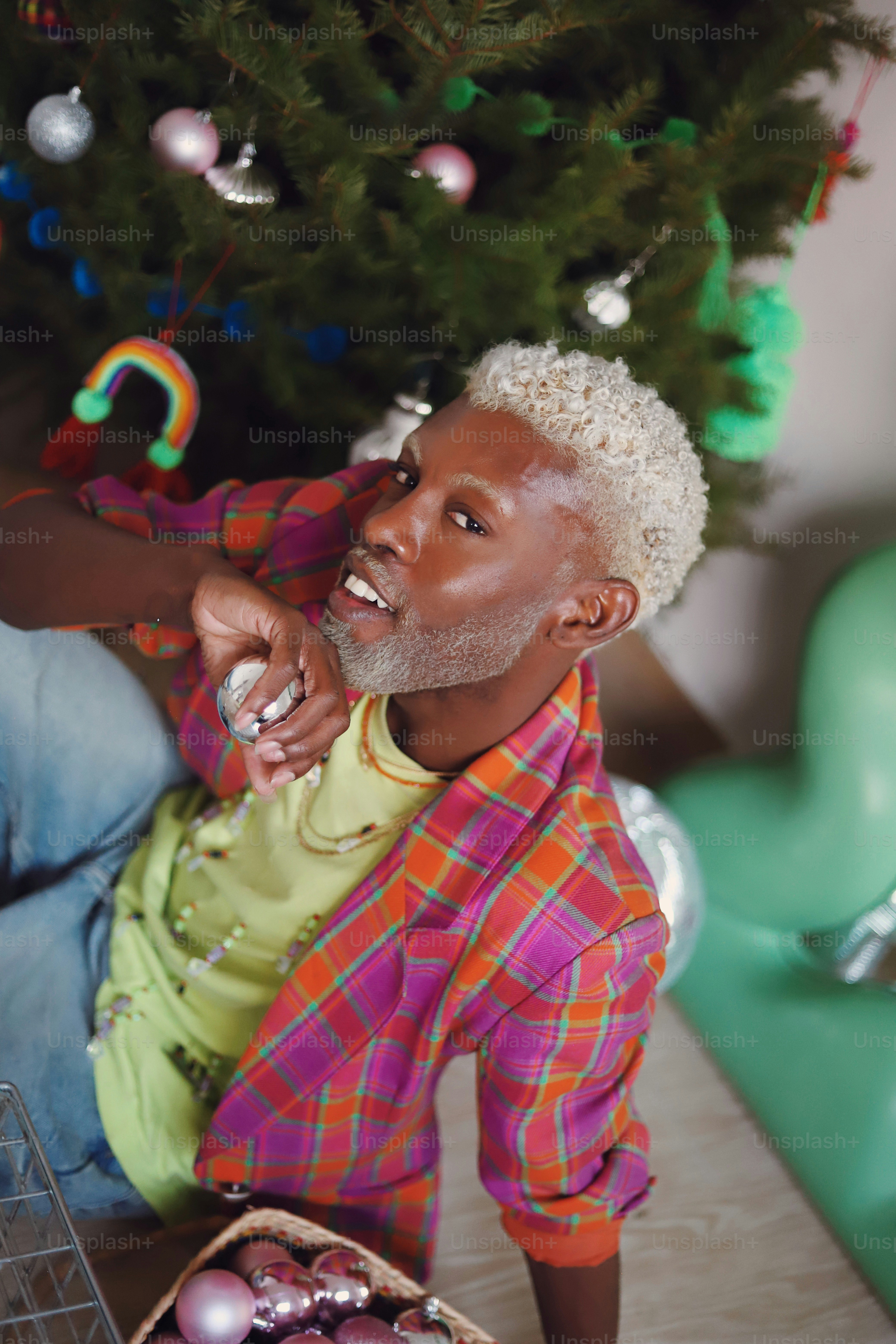 A man sitting next to a christmas tree holding a wine glass
