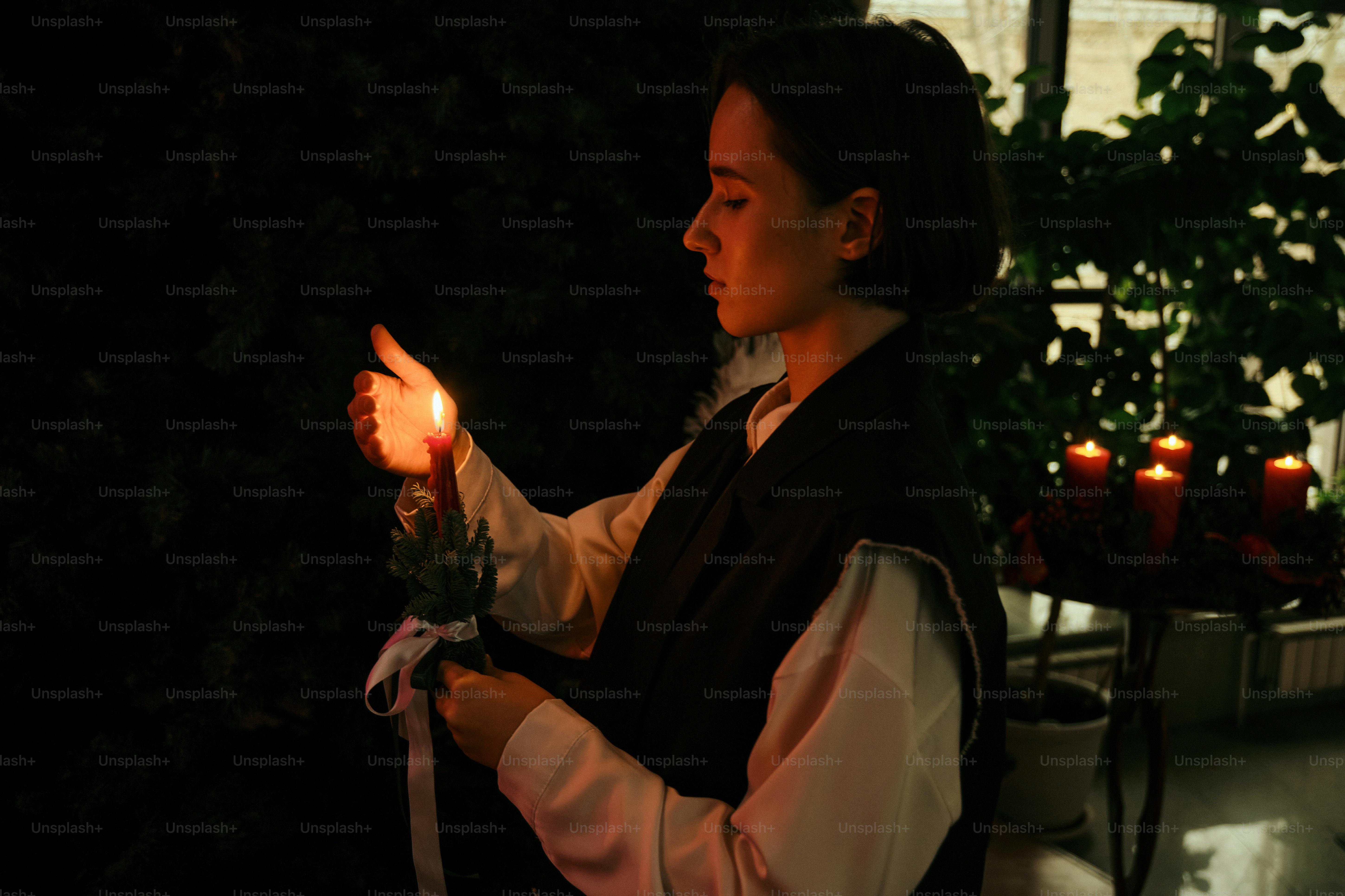 暗い部屋で火のついたろうそくを持つ女性