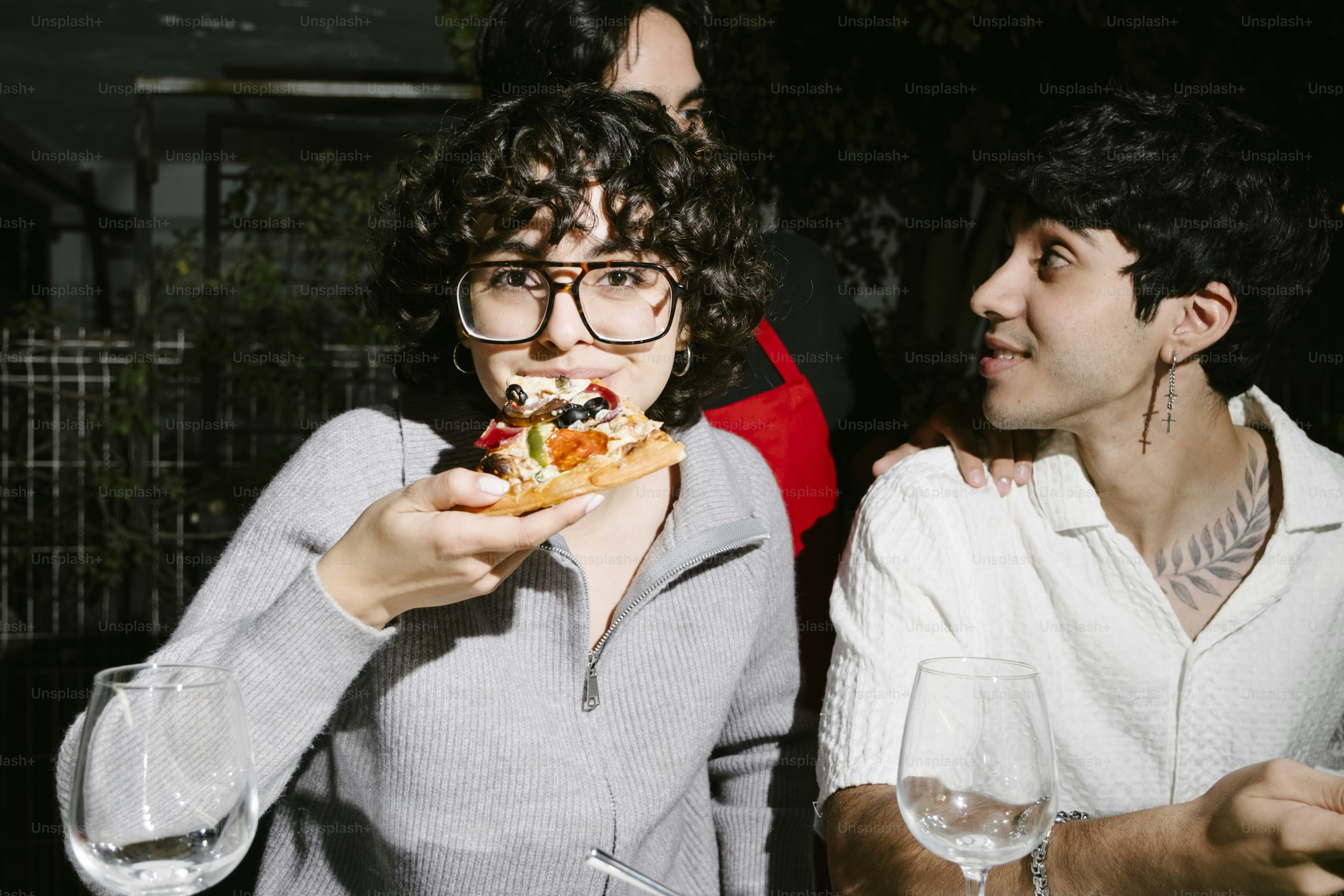 A woman eating a piece of pizza while standing next to a man