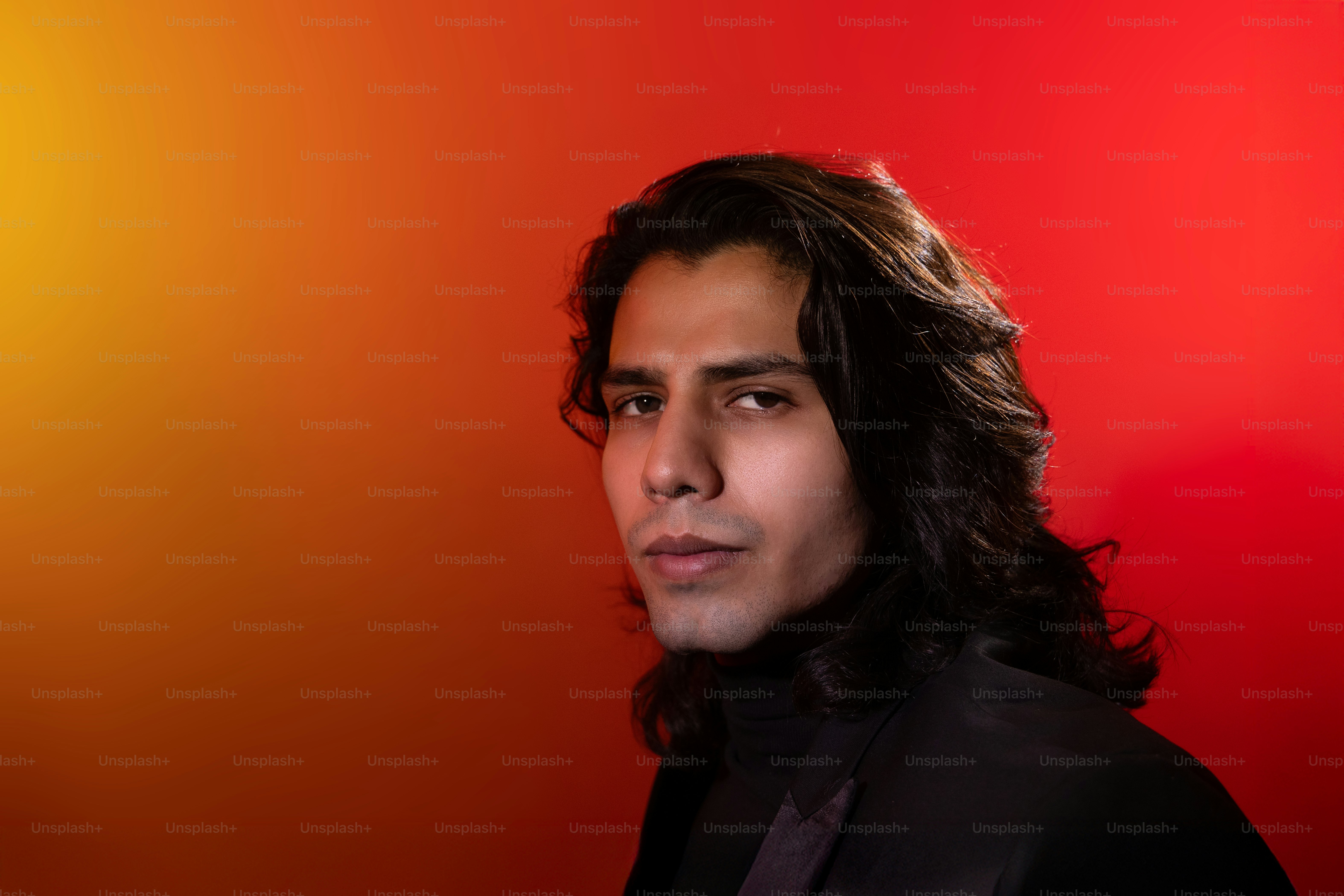 Um homem com cabelo comprido em pé na frente de um fundo vermelho e amarelo