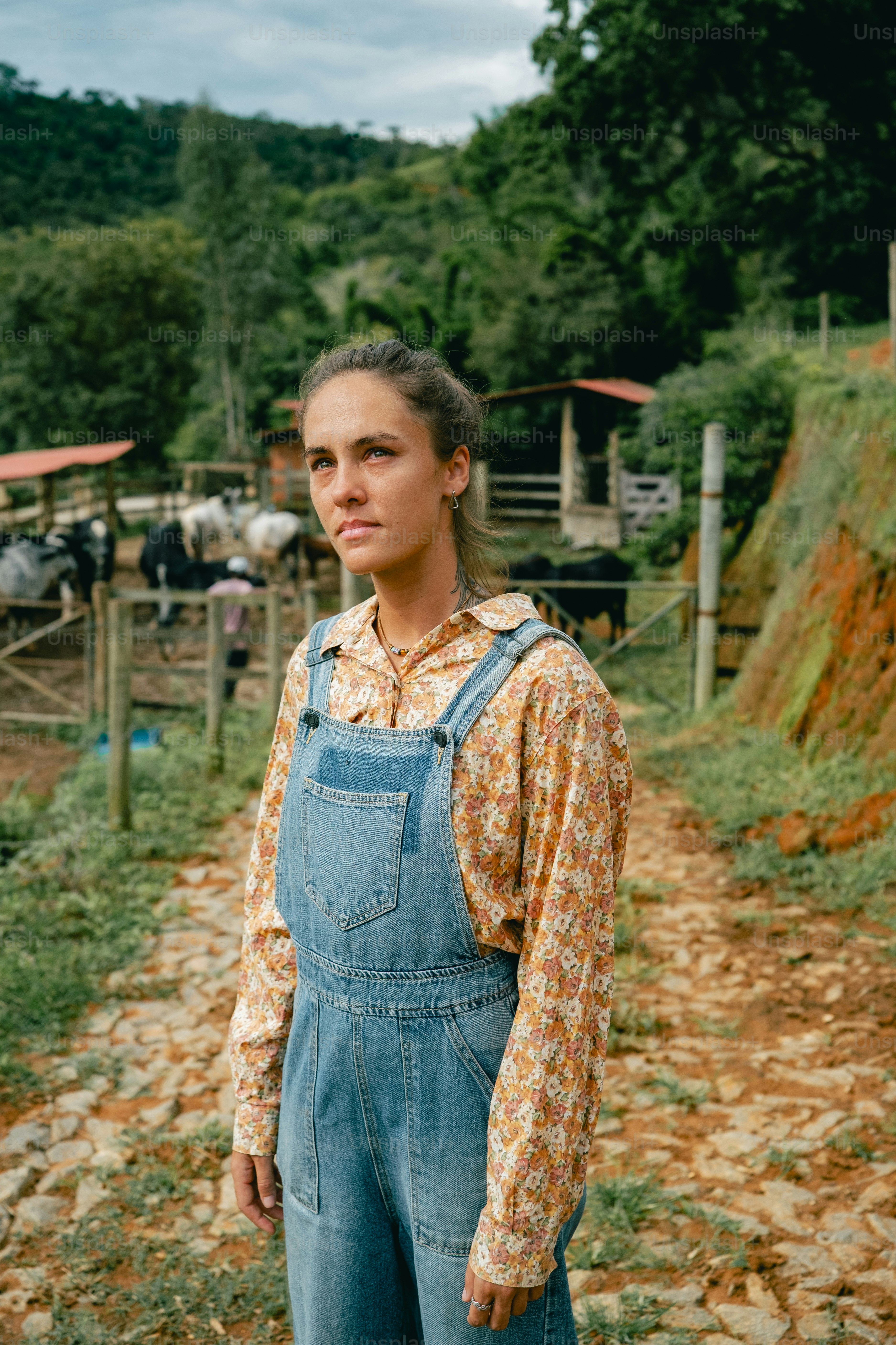 A woman in overalls standing in front of a farm