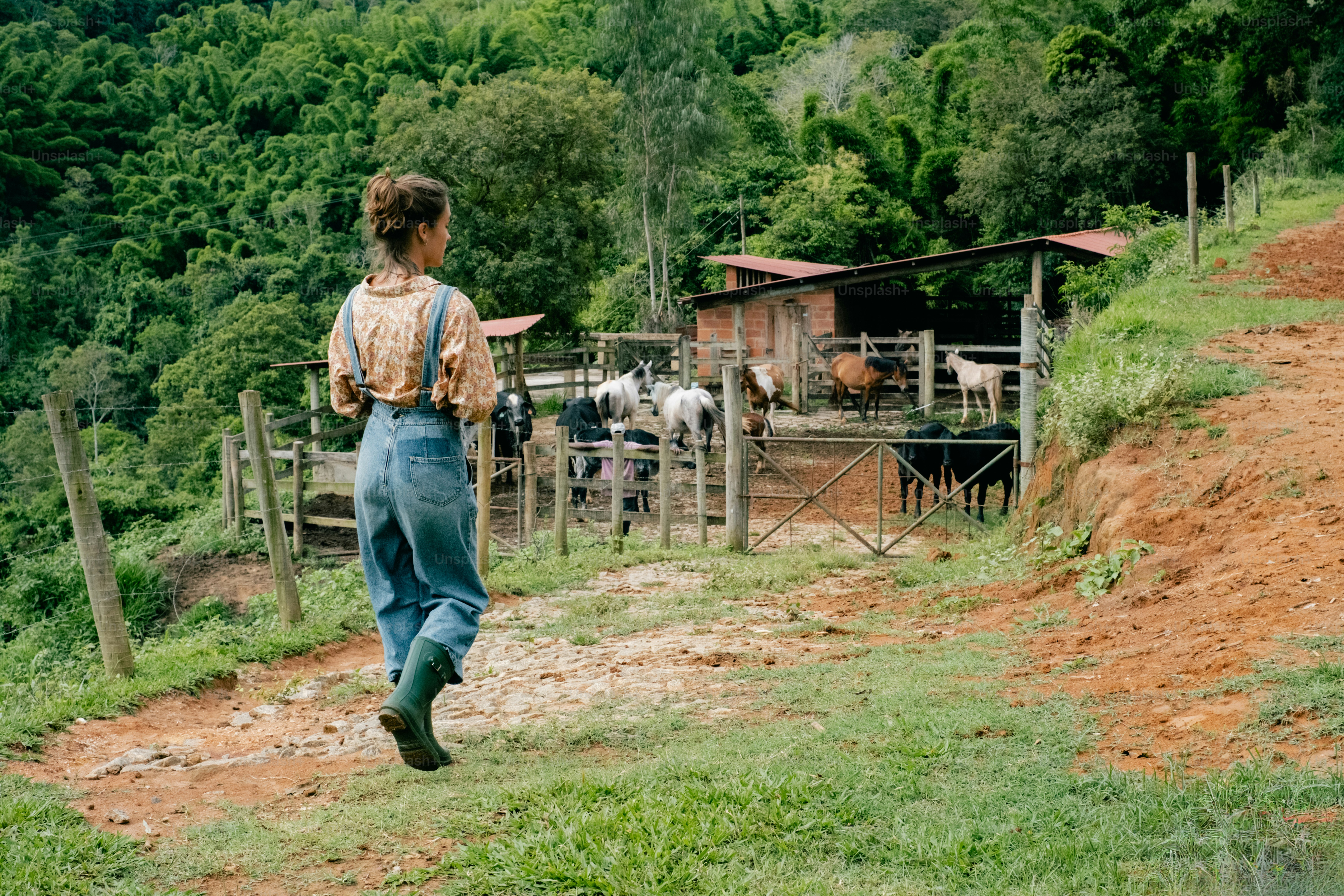 A woman walking down a dirt road next to a lush green hillside