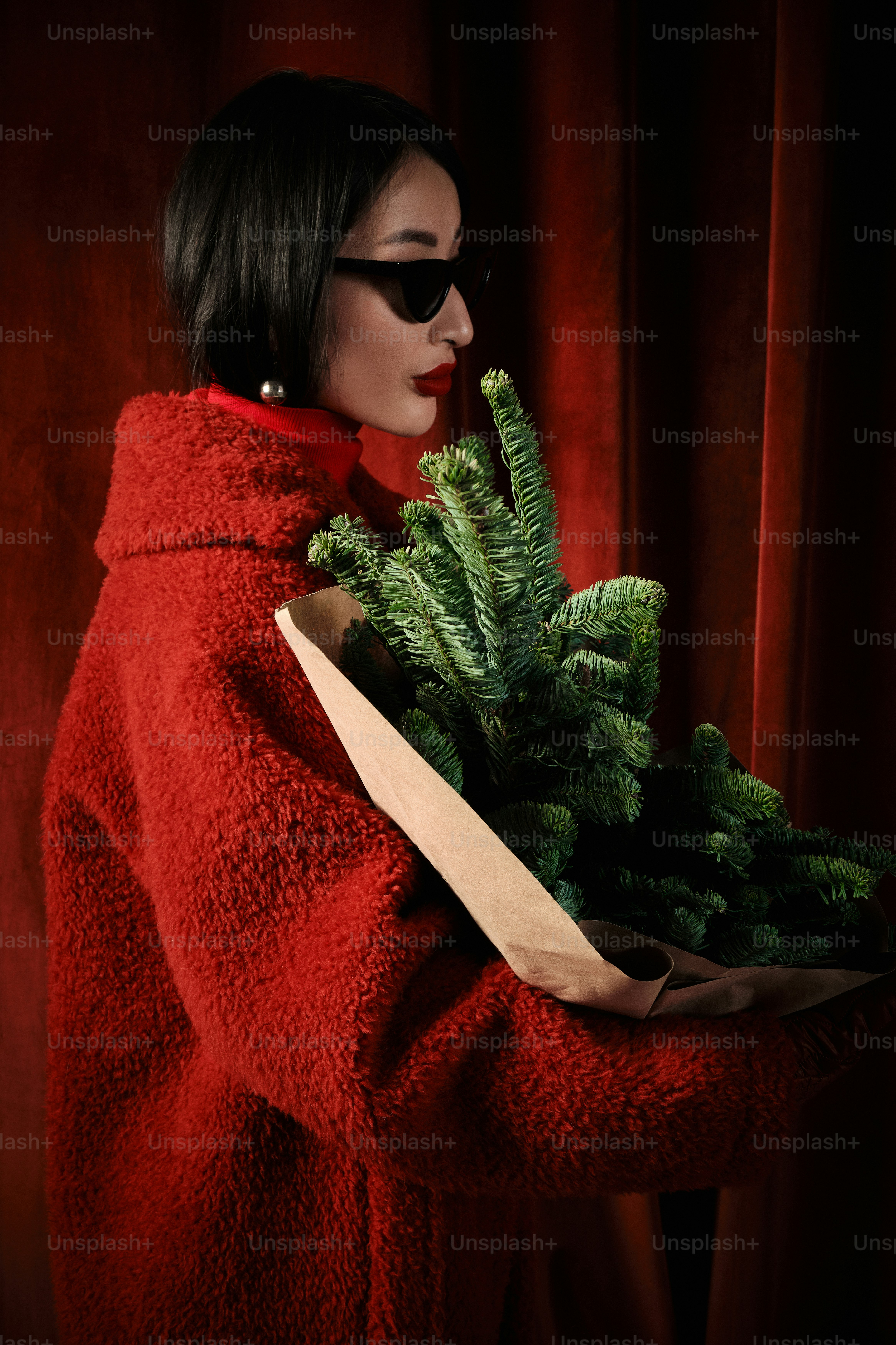 Eine Frau in einem roten Mantel hält einen Weihnachtsbaum in der Hand