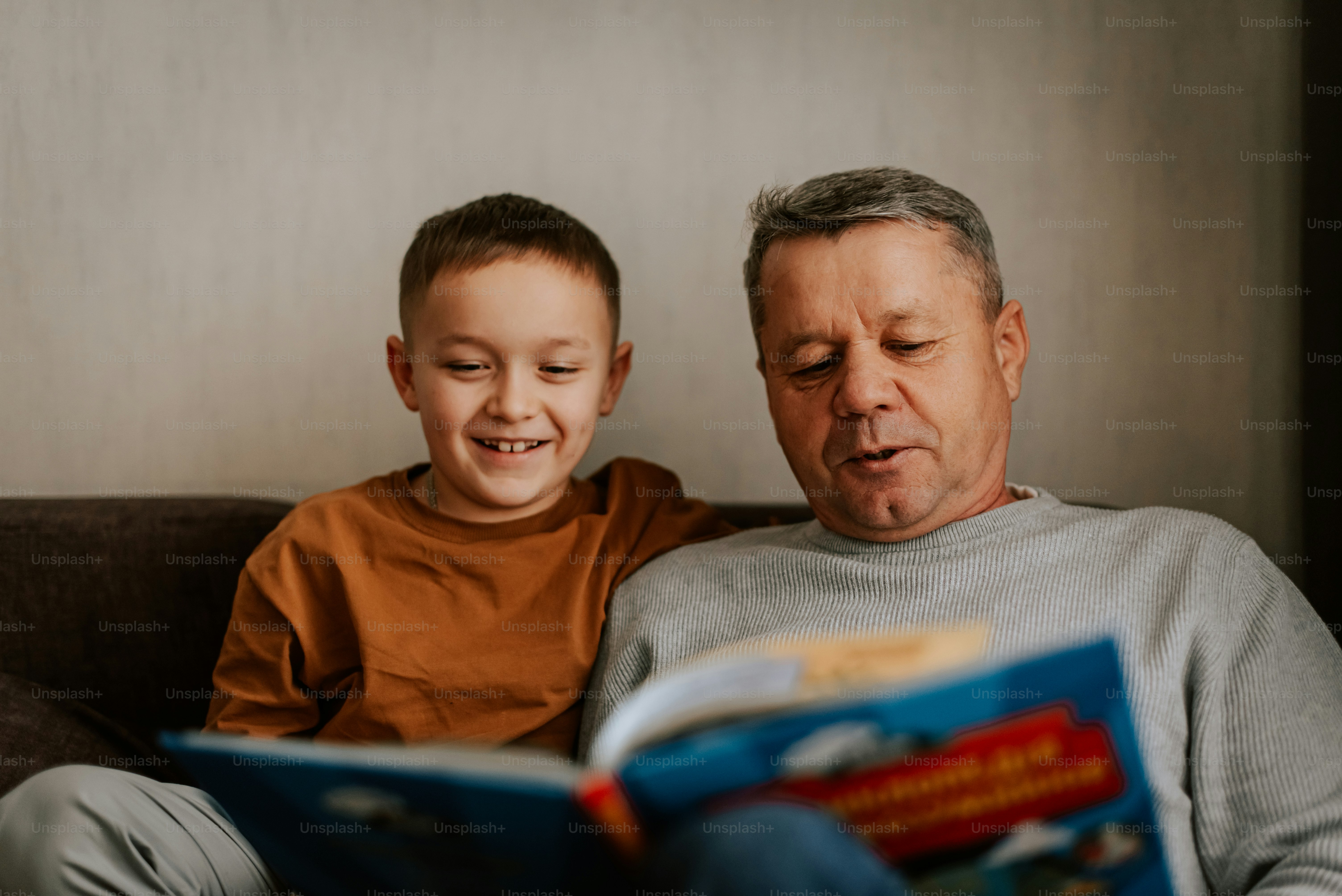 A man and a boy sitting on a couch reading a book
