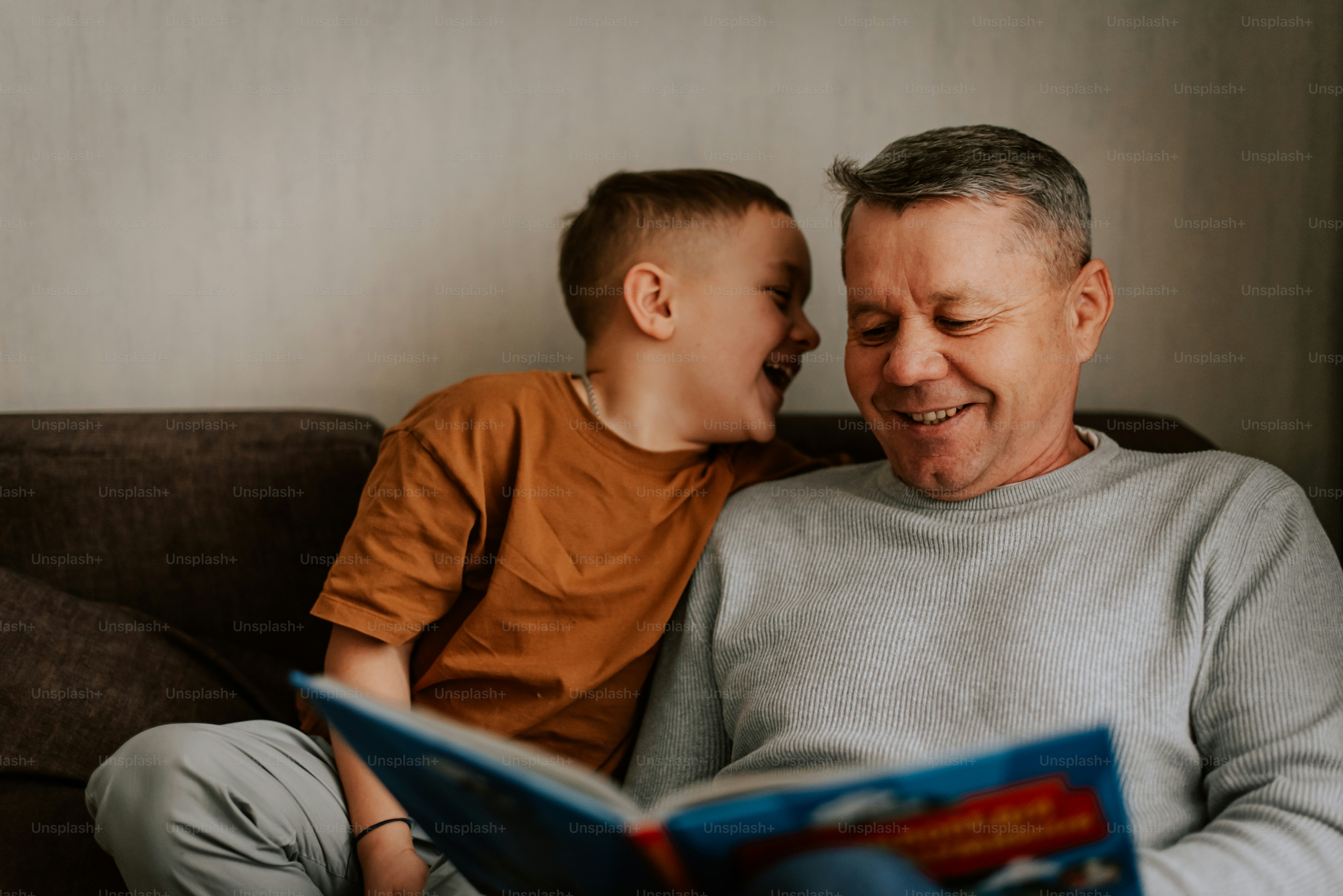 A man and a boy sitting on a couch reading a book