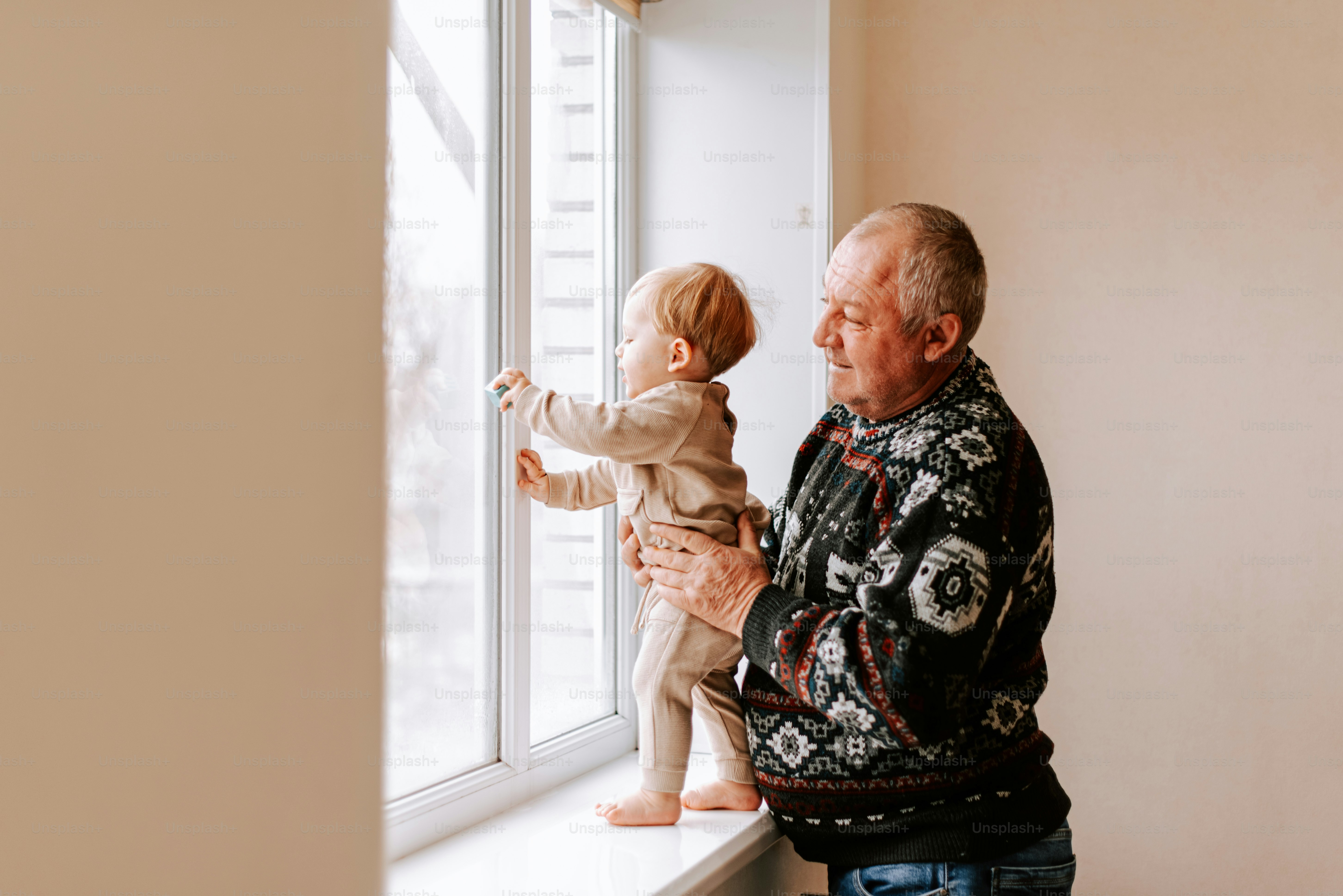 An older man holding a toddler looking out a window