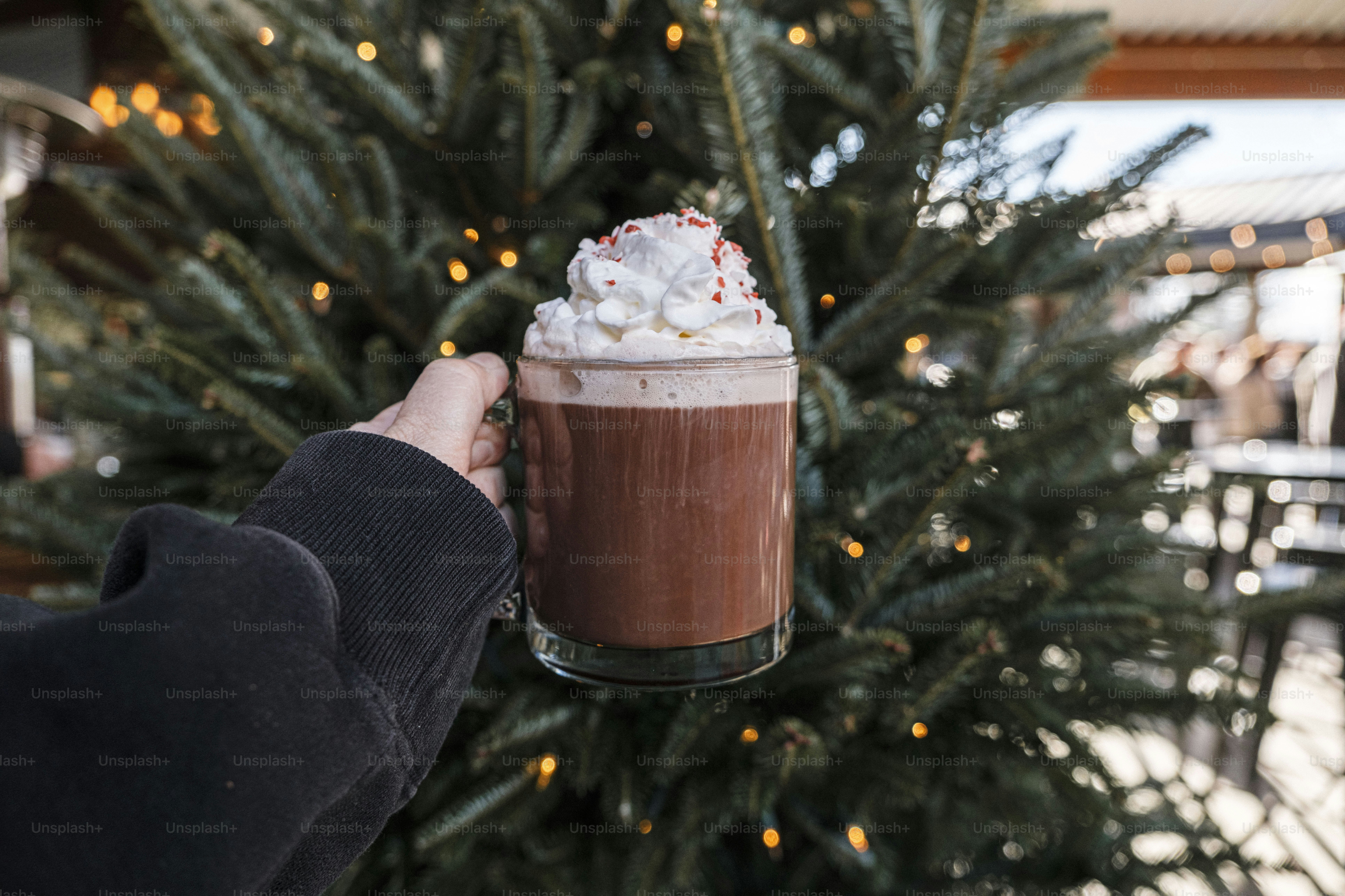 A person holding a drink in front of a christmas tree