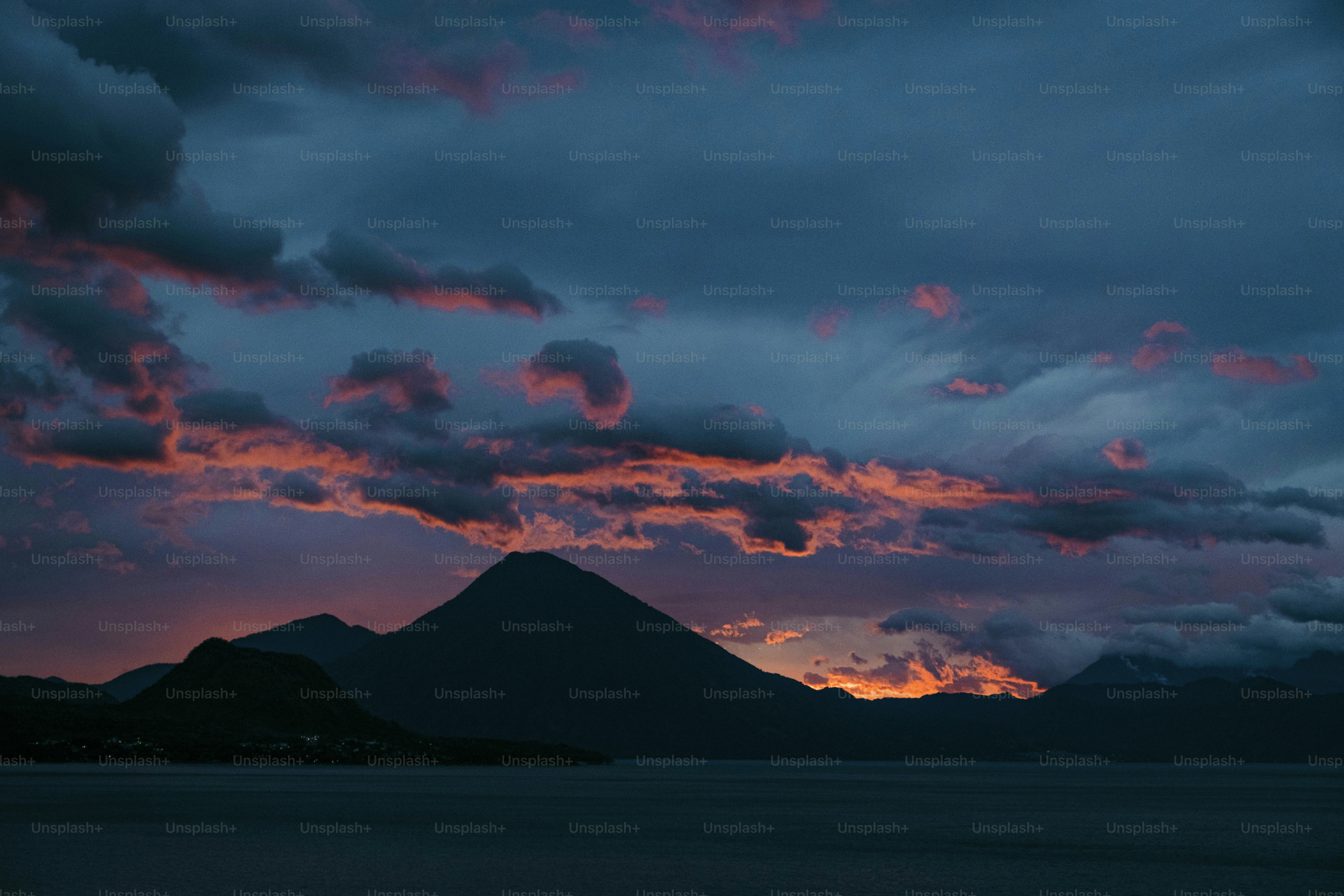 Un atardecer con nubes y una montaña de fondo