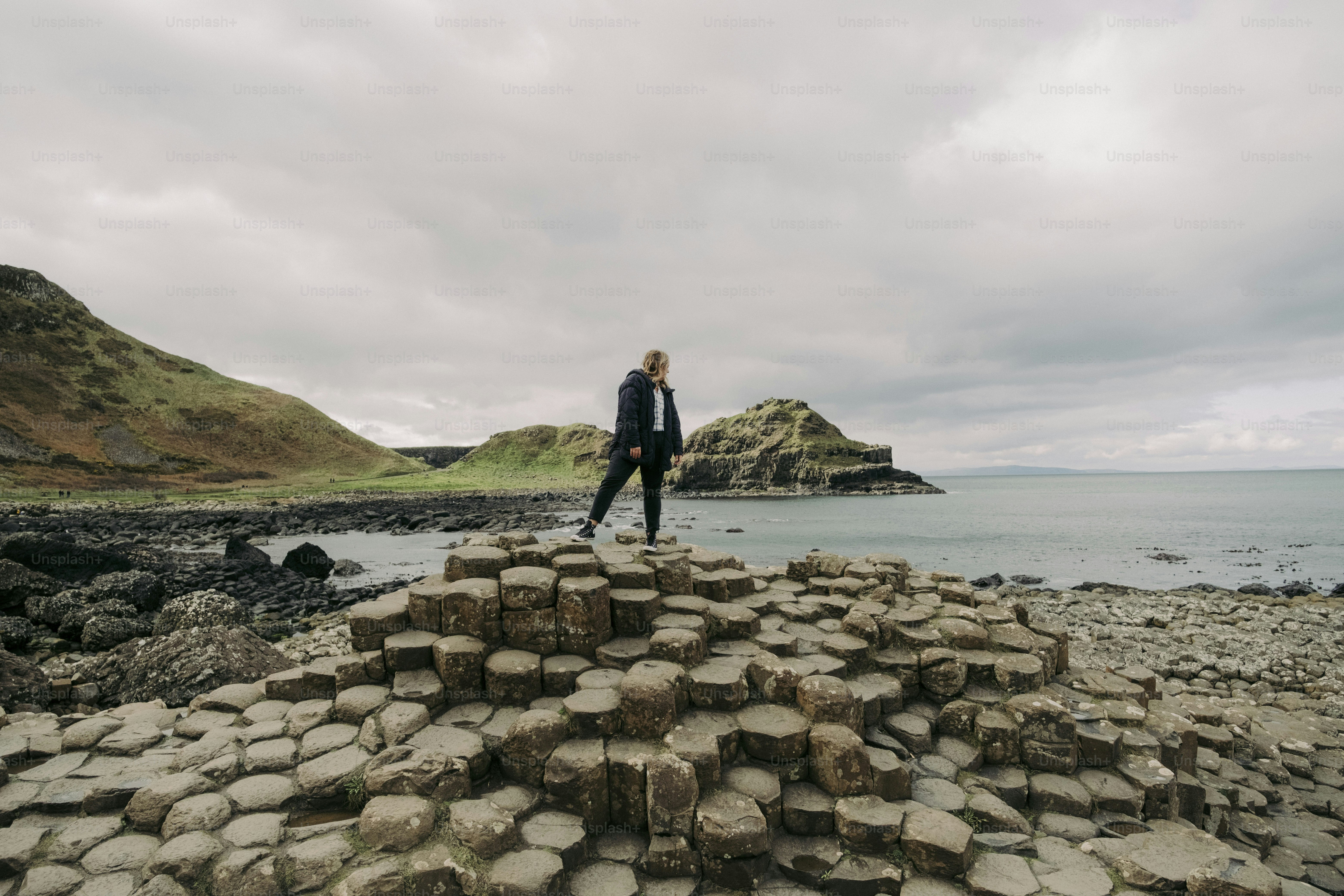 A man standing on top of a pile of rocks near the ocean