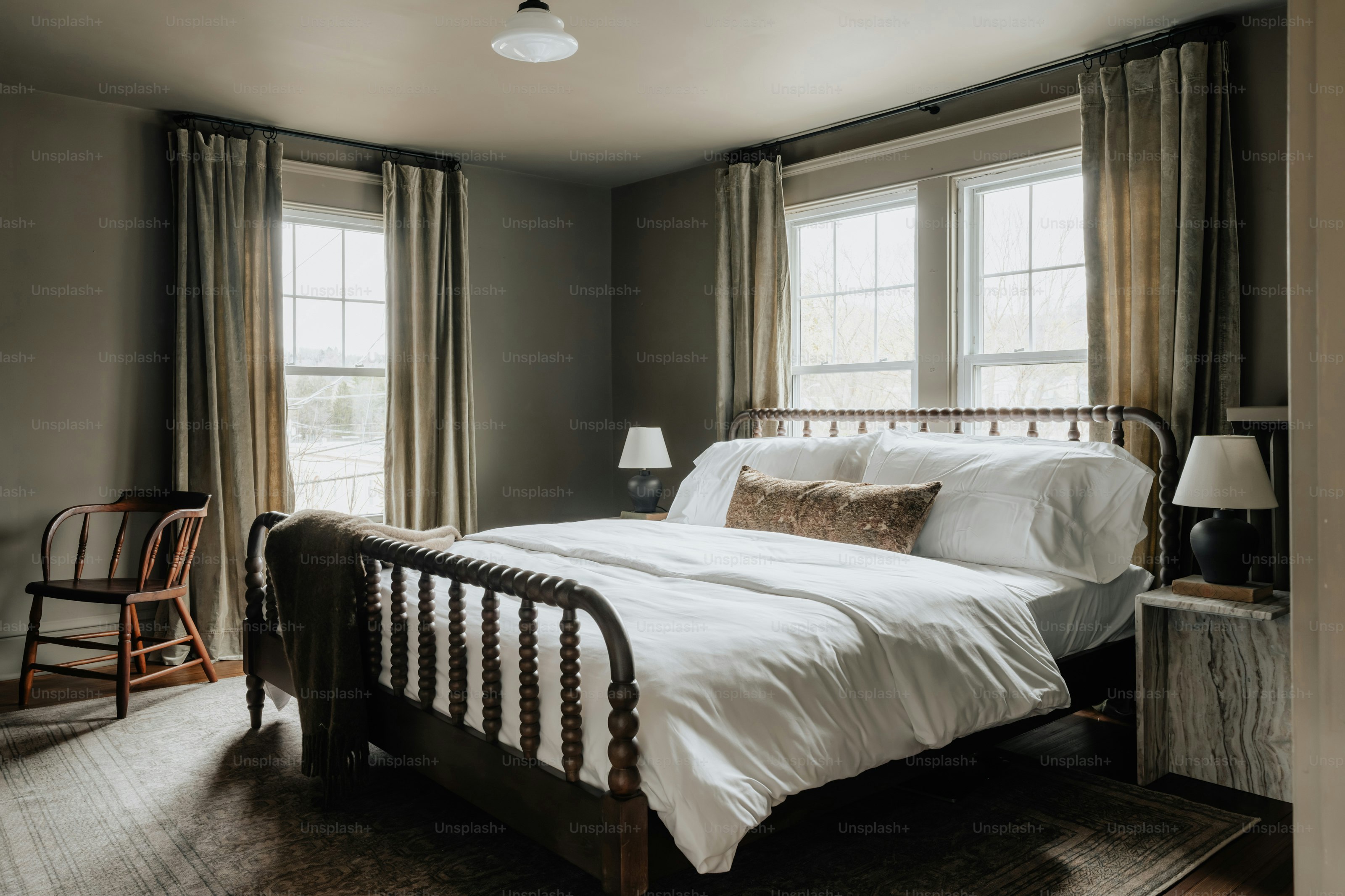 Una cama en un dormitorio junto a dos ventanas