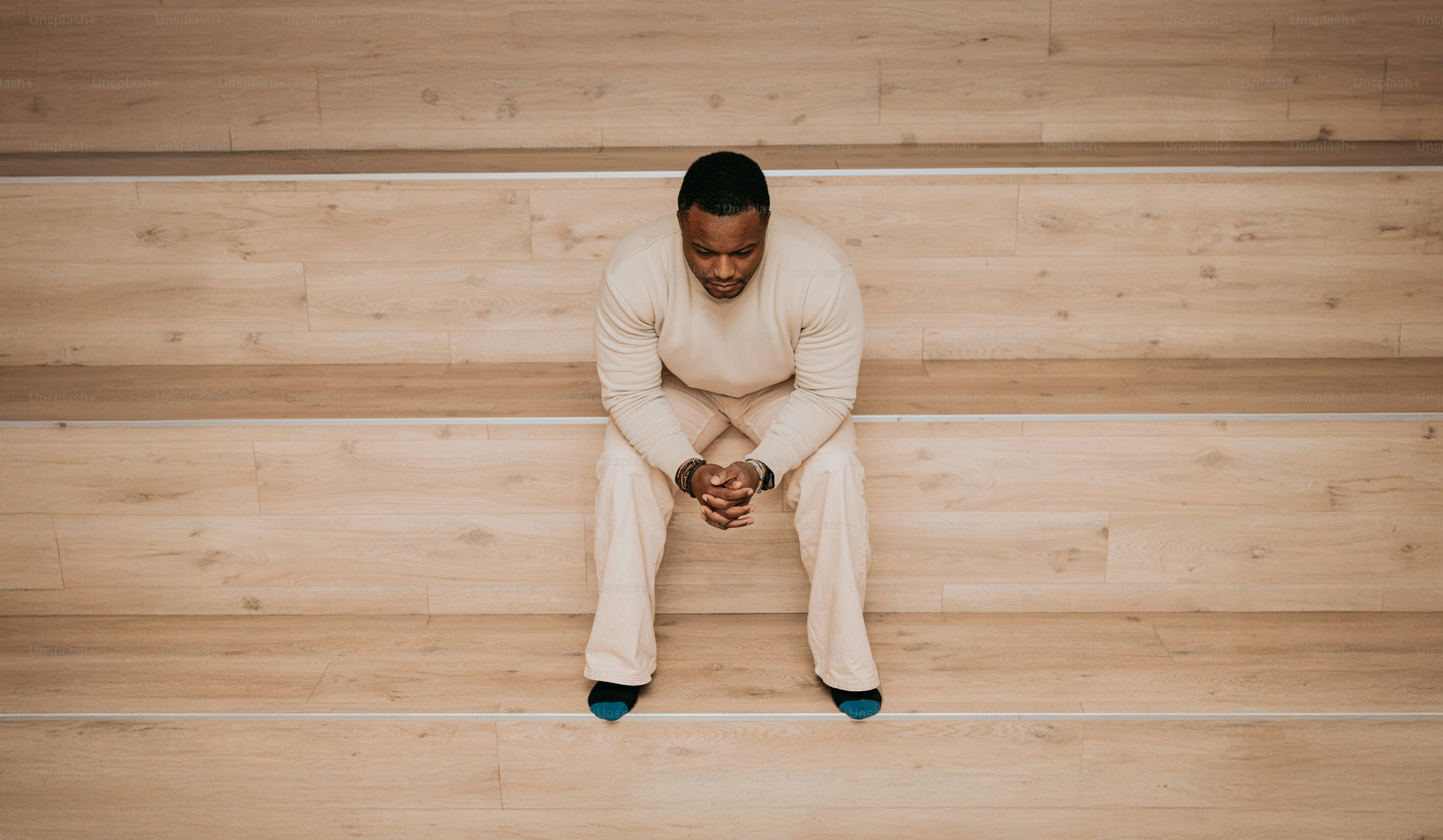 Seorang pria duduk di lantai kayu dengan kaki disilangkan
