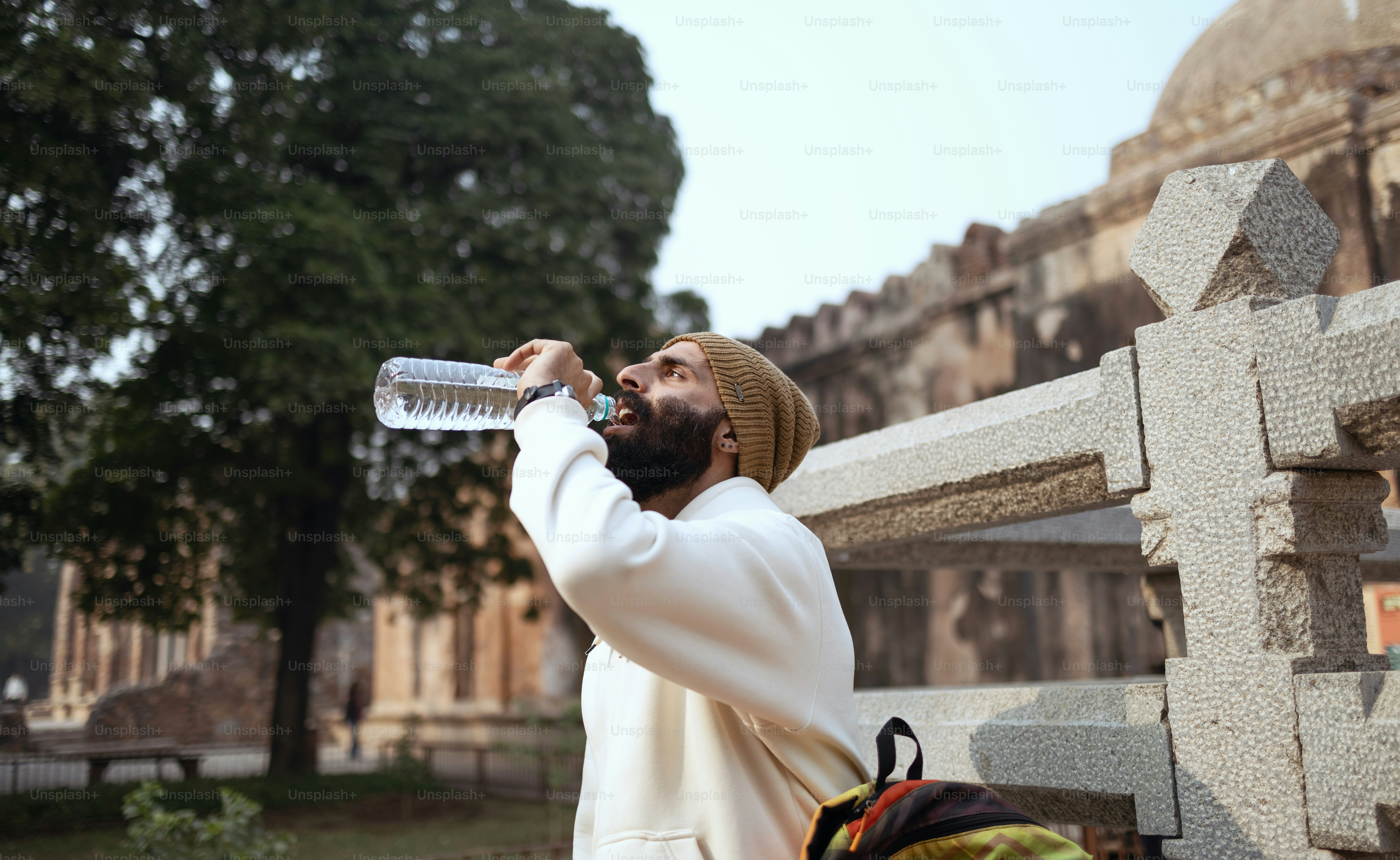 A man in a white robe is drinking from a water bottle