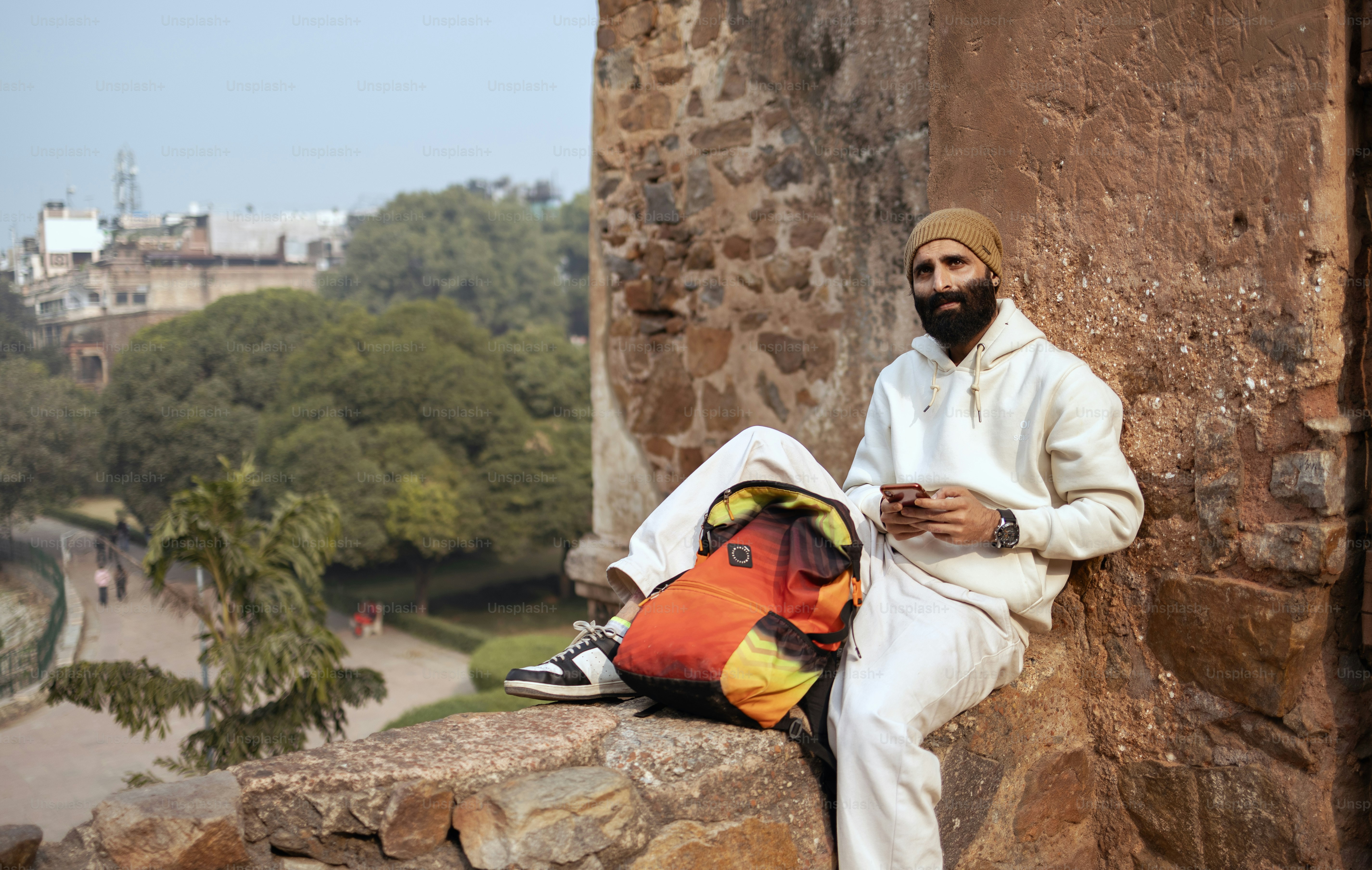 Un hombre sentado en un muro de piedra junto a una bolsa