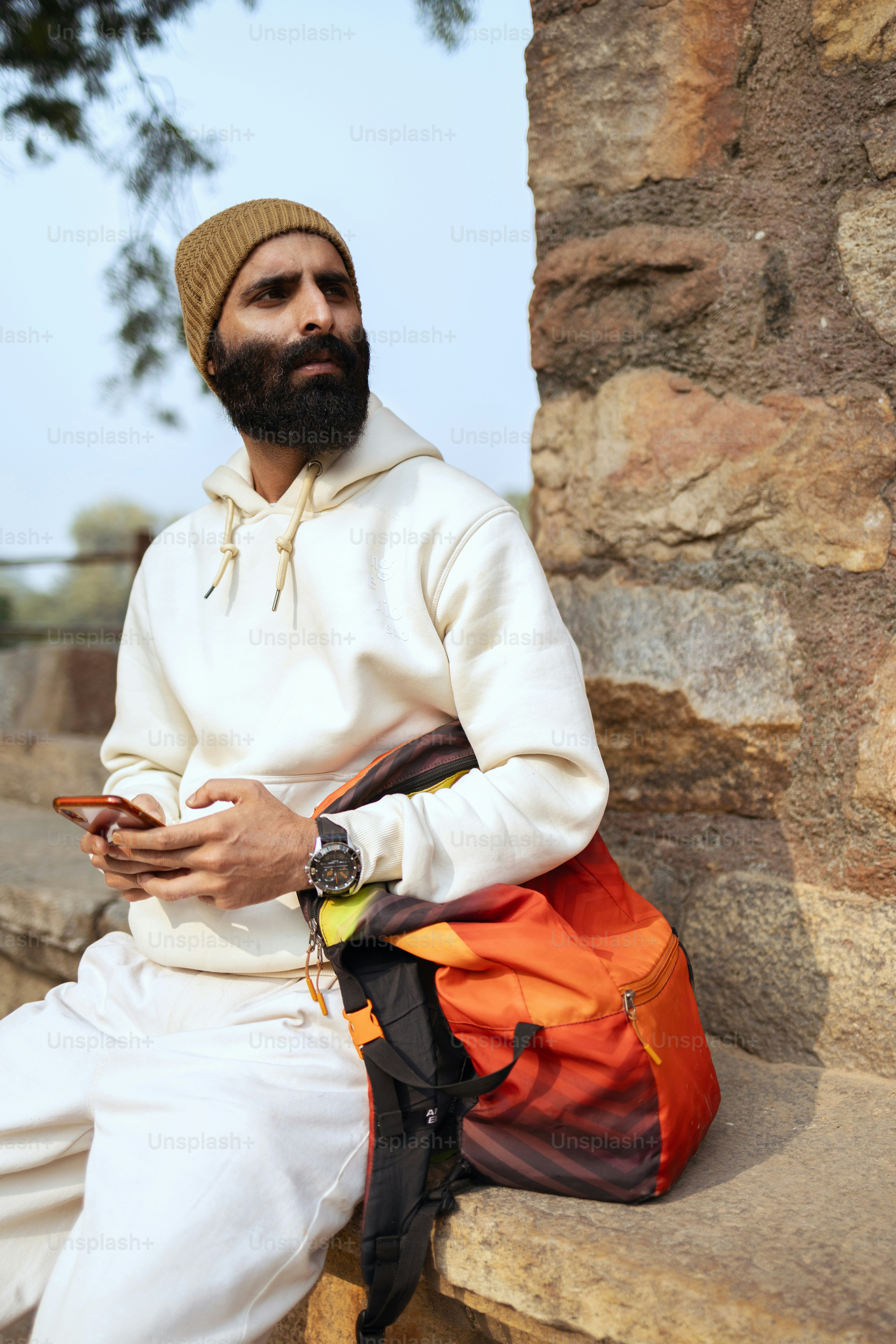 A man sitting on a stone wall looking at his cell phone