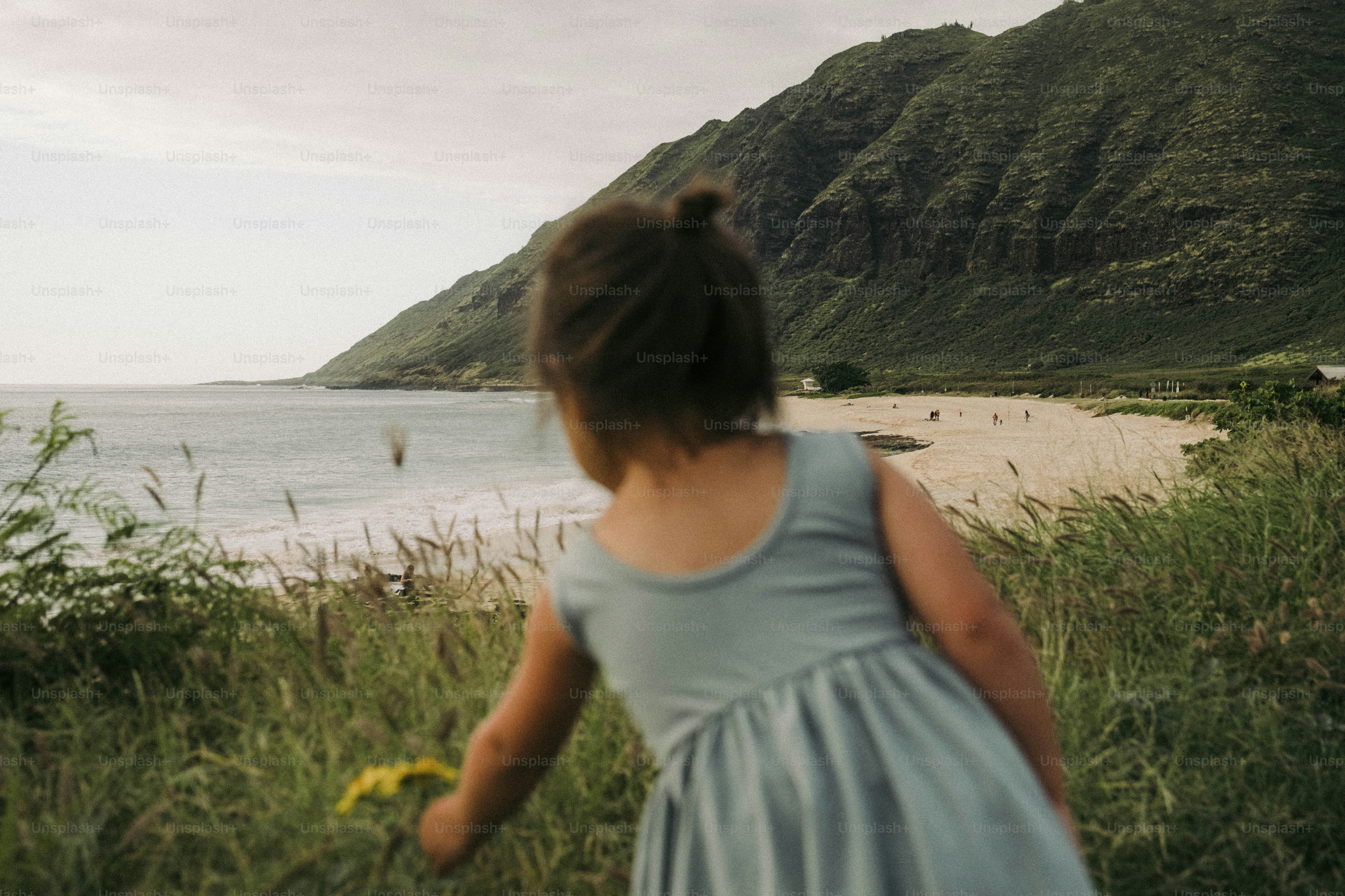 A little girl in a blue dress walking by the ocean