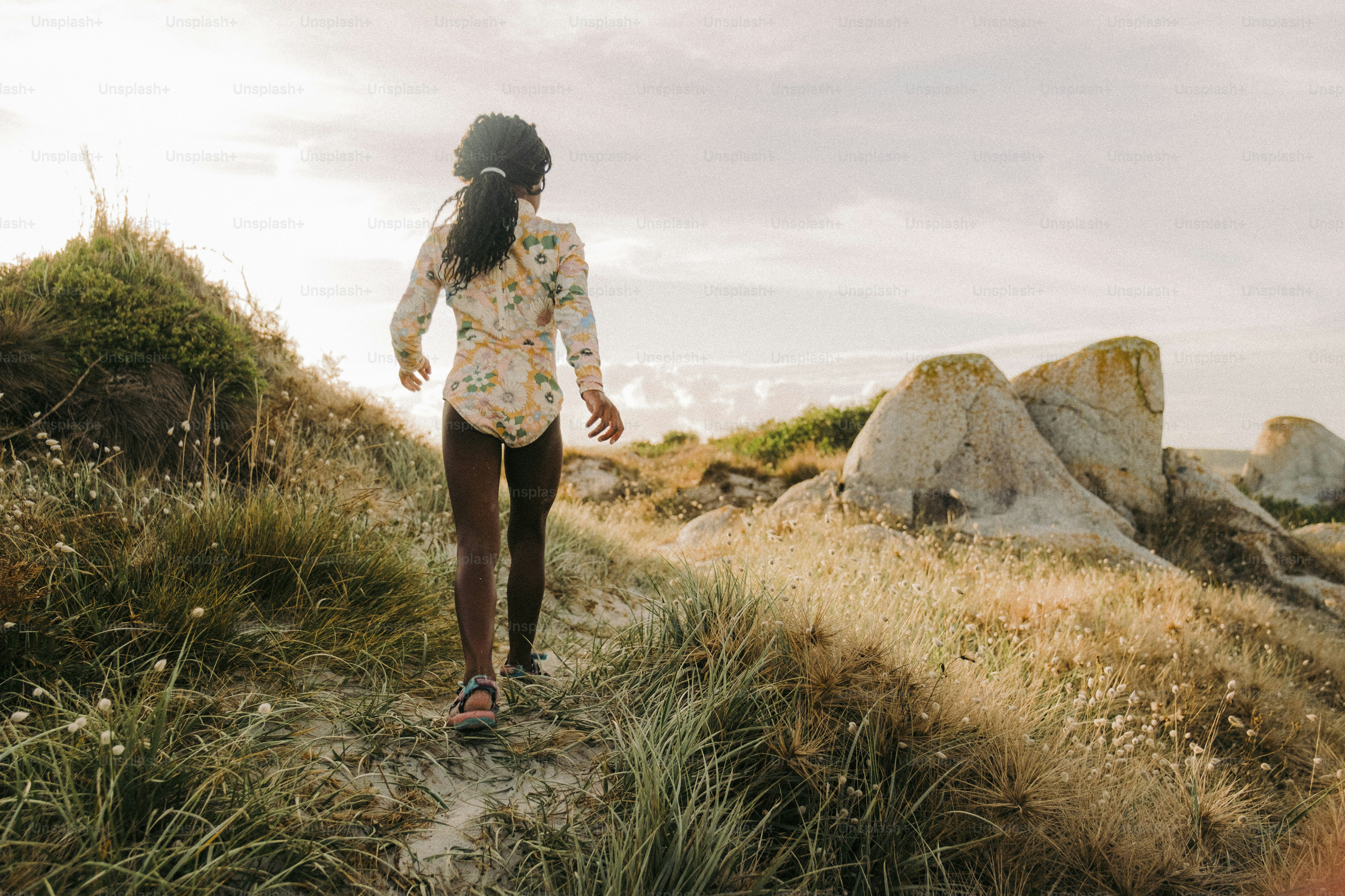 Eine Frau, die einen Feldweg neben hohem Gras entlanggeht