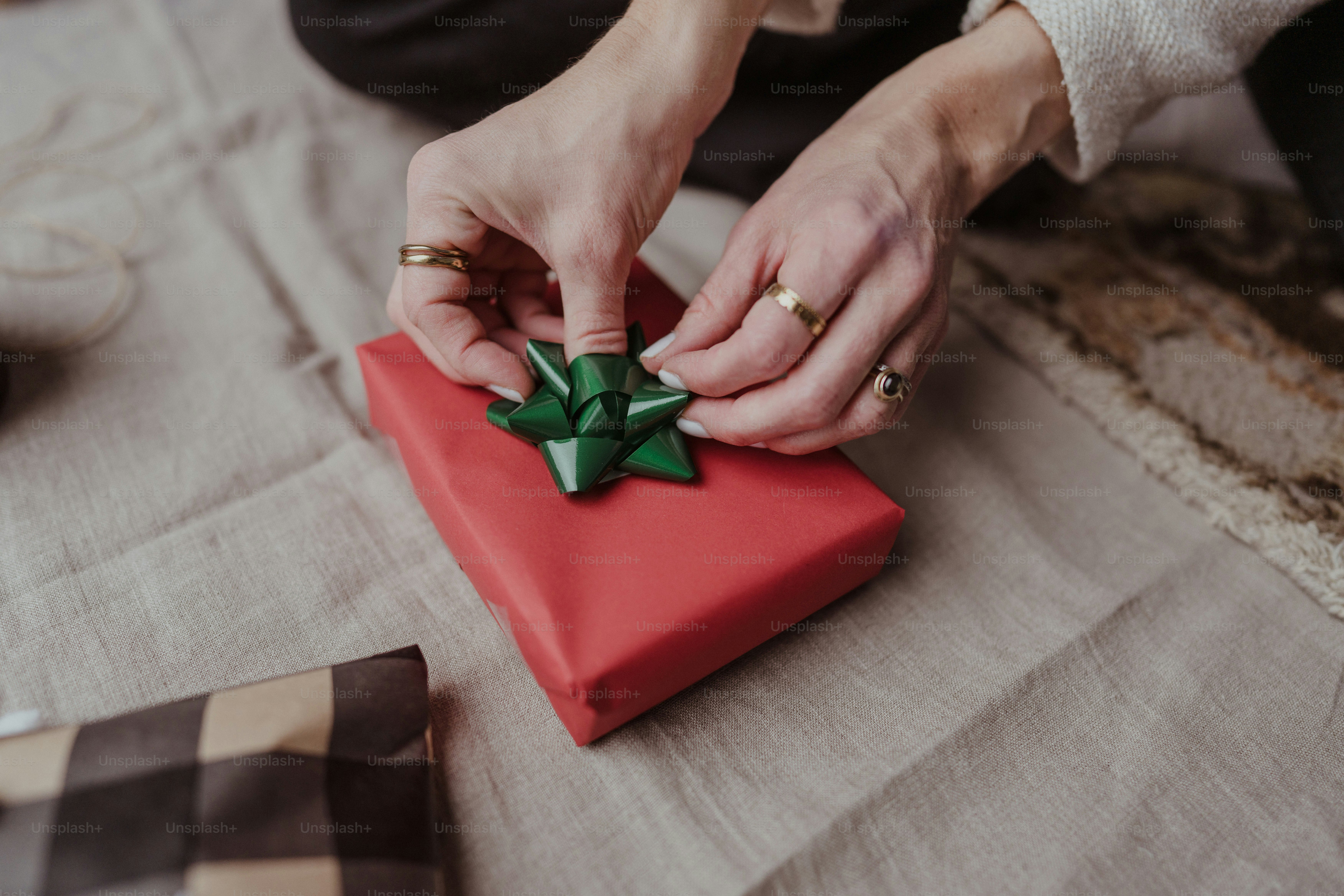 A woman is wrapping a red present with a green bow