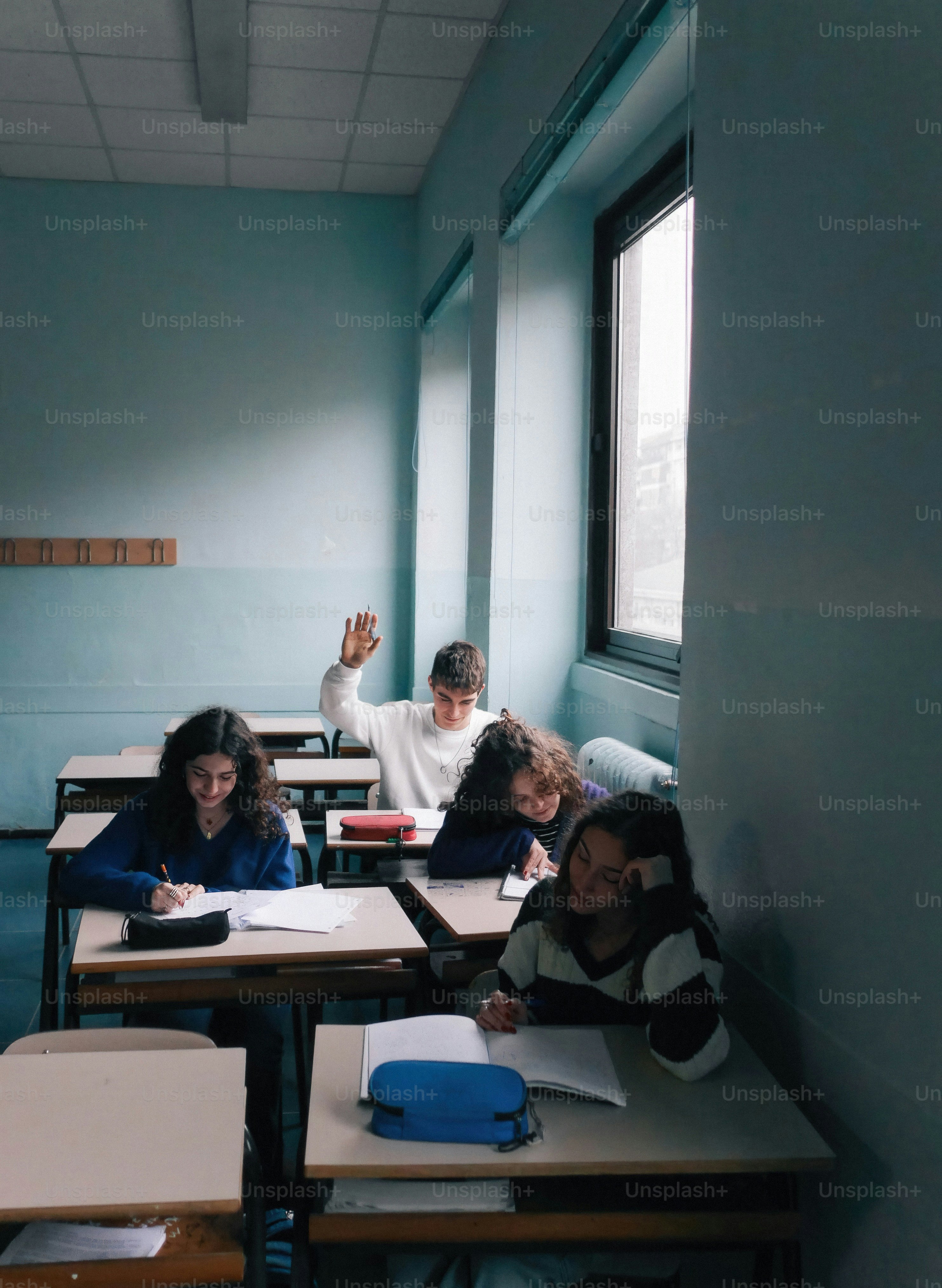 A group of children sitting at desks in a classroom photo – Raised hand ...