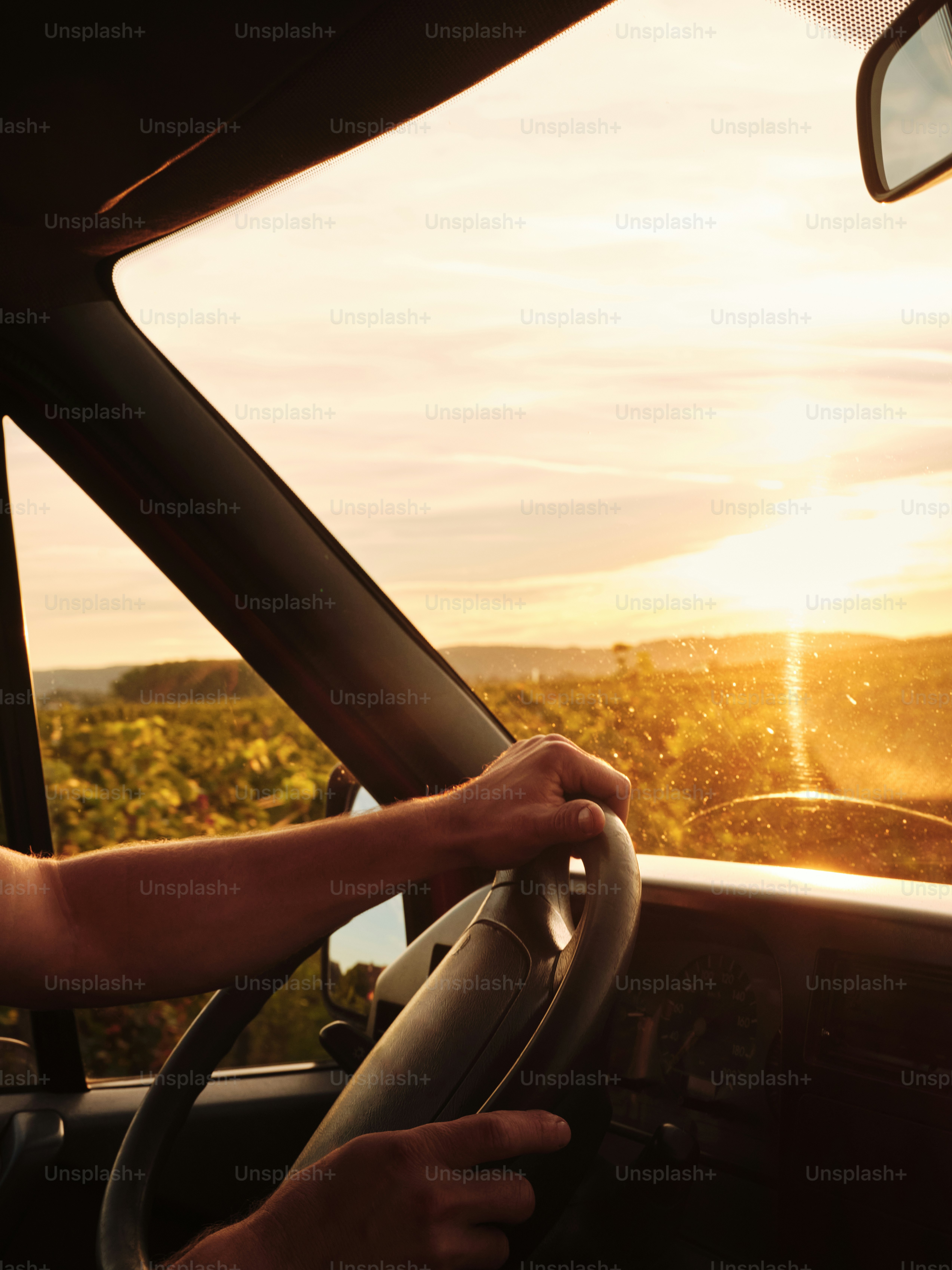A man driving a car with the sun setting in the background