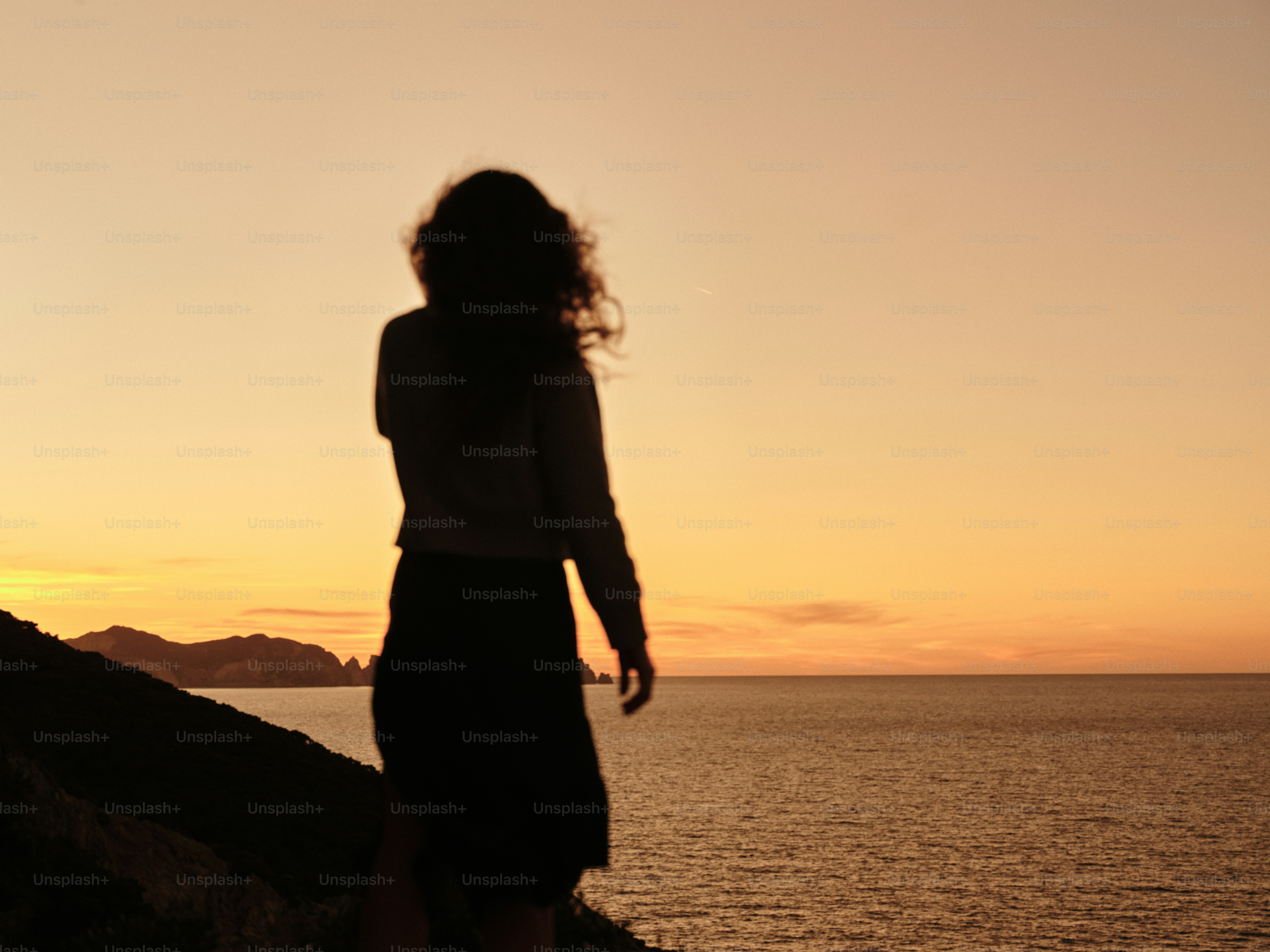 A woman standing on top of a cliff next to the ocean