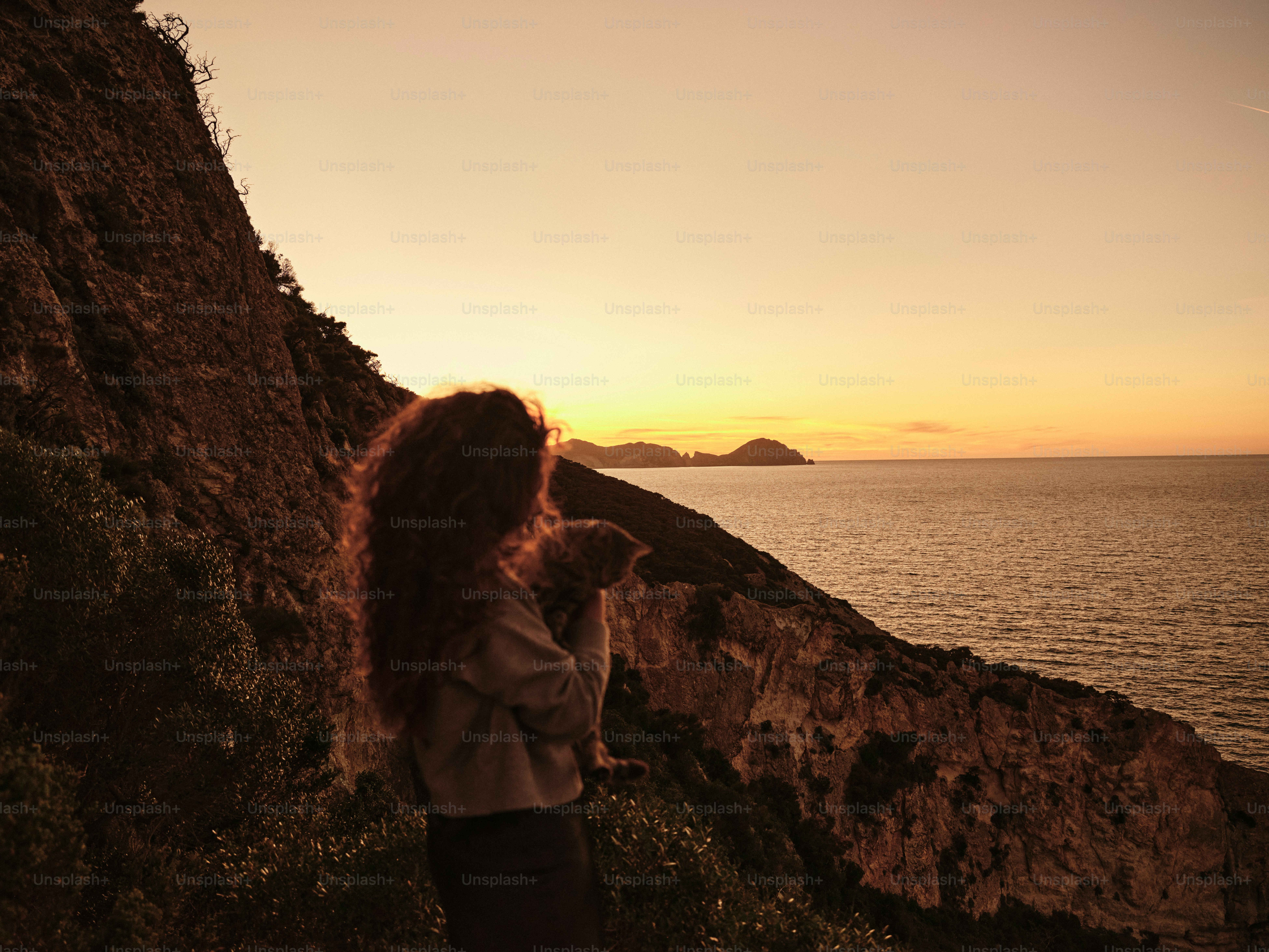 Uma mulher em pé ao lado de um penhasco ao lado do oceano
