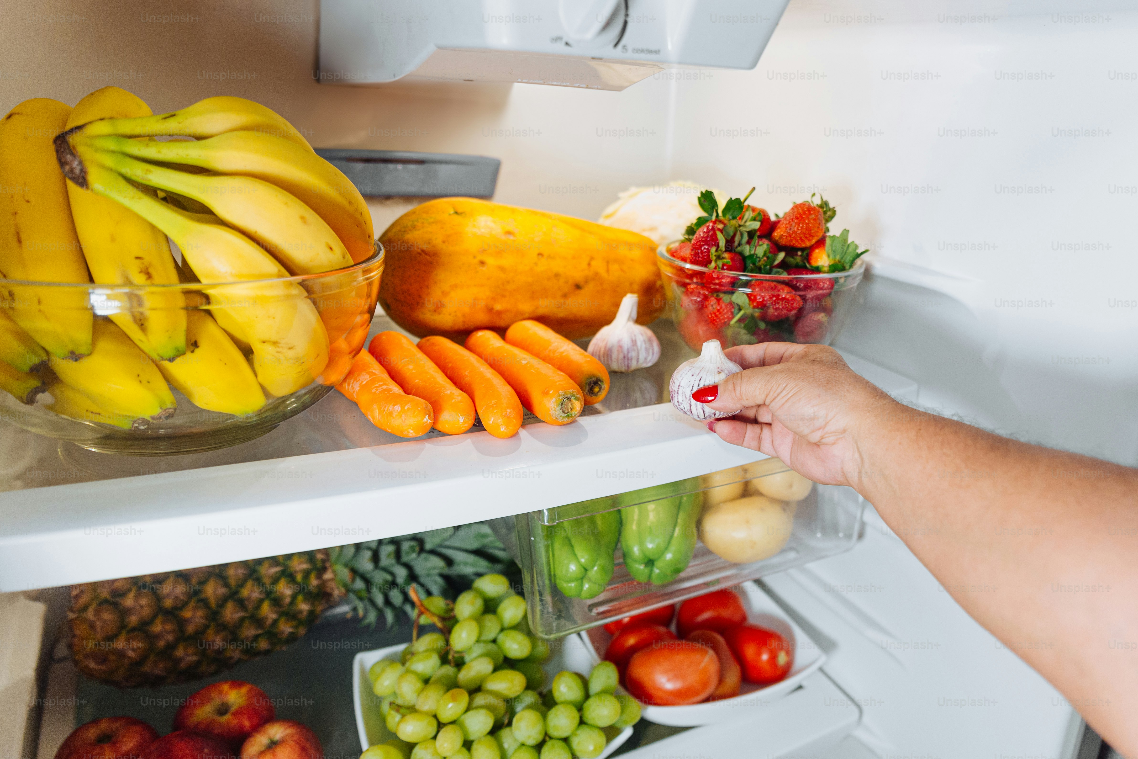 A woman reaching into a refrigerator filled with fruits and vegetables