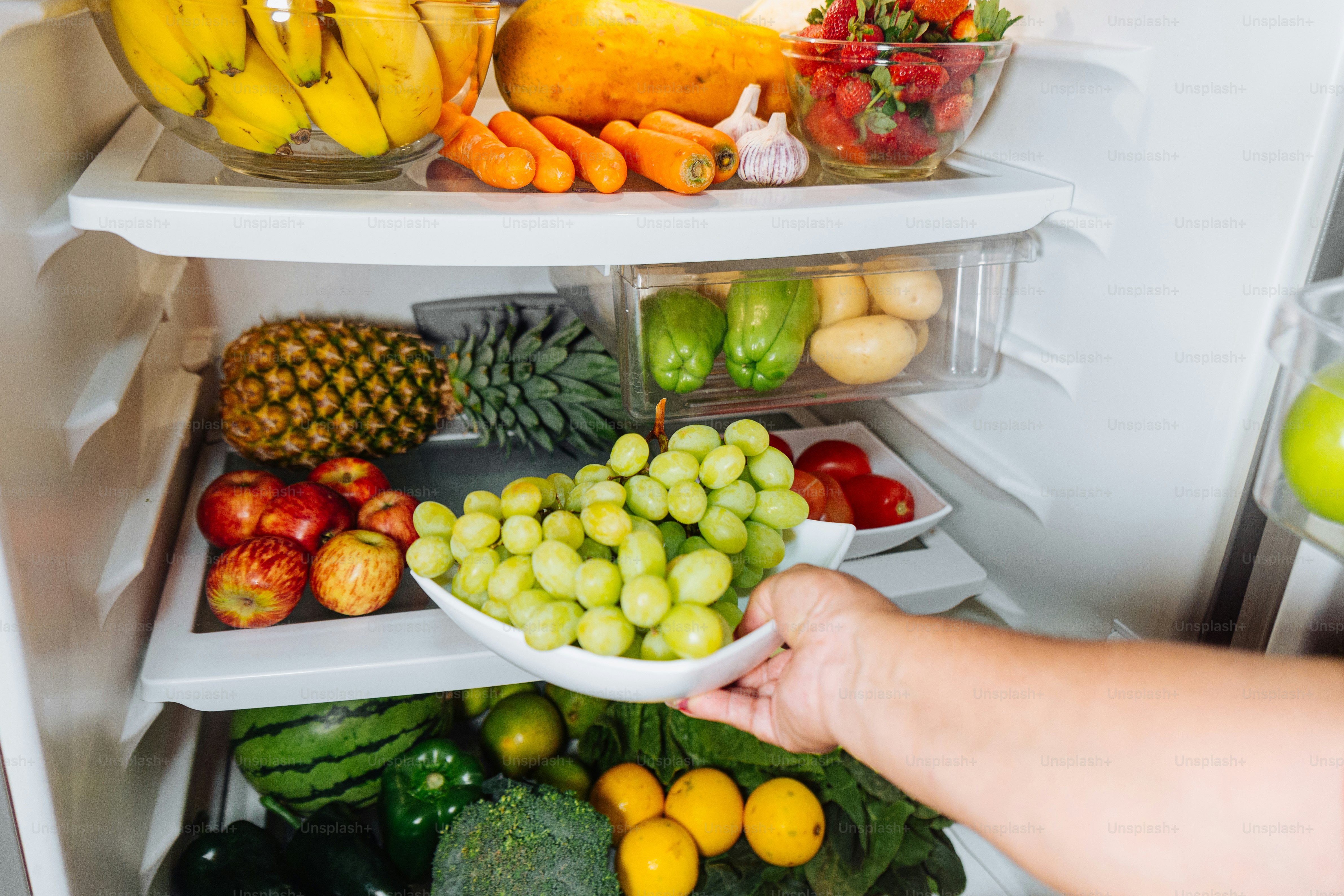 A person holding a bowl of fruit in front of an open refrigerator