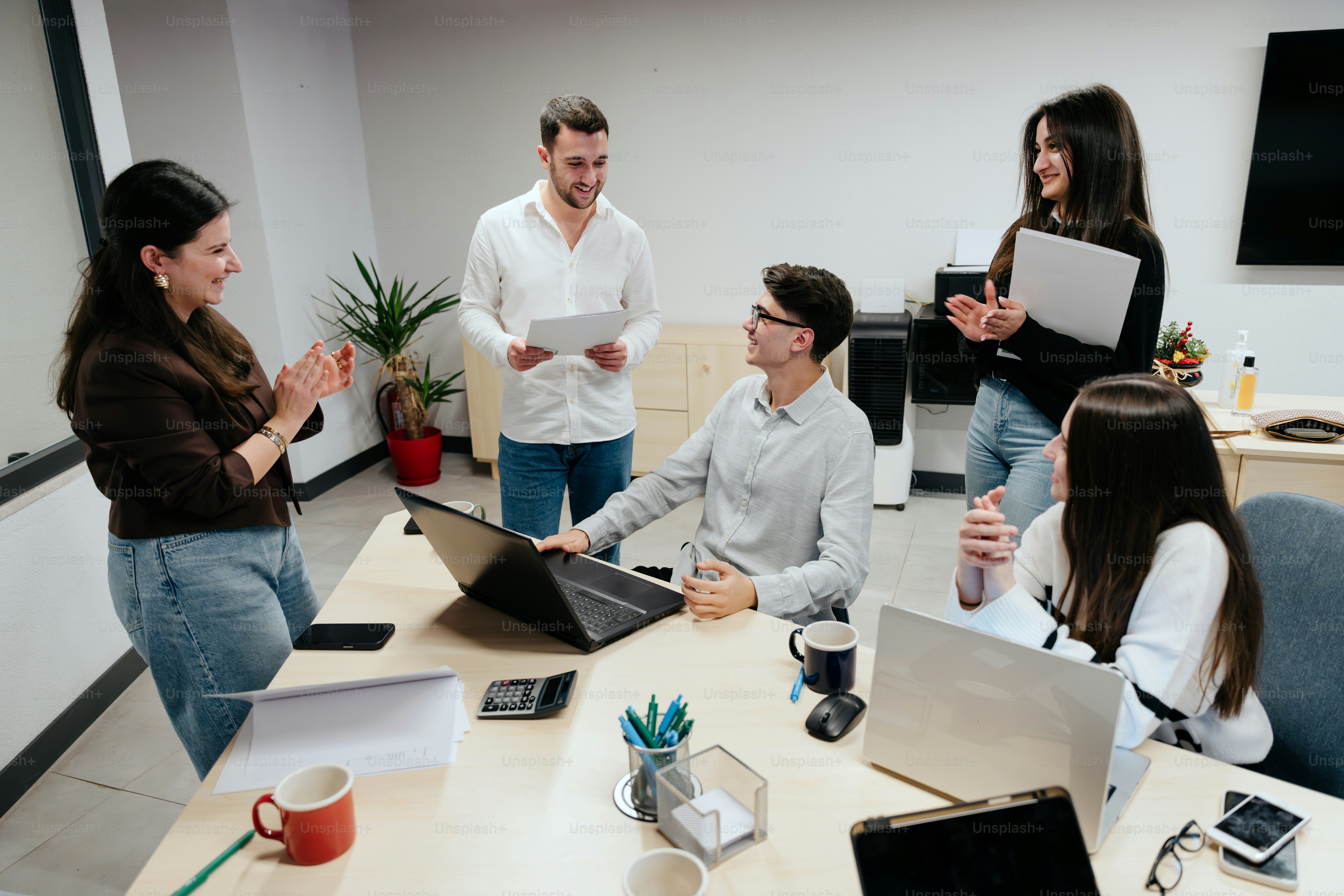 A group of people sitting around a table with laptops