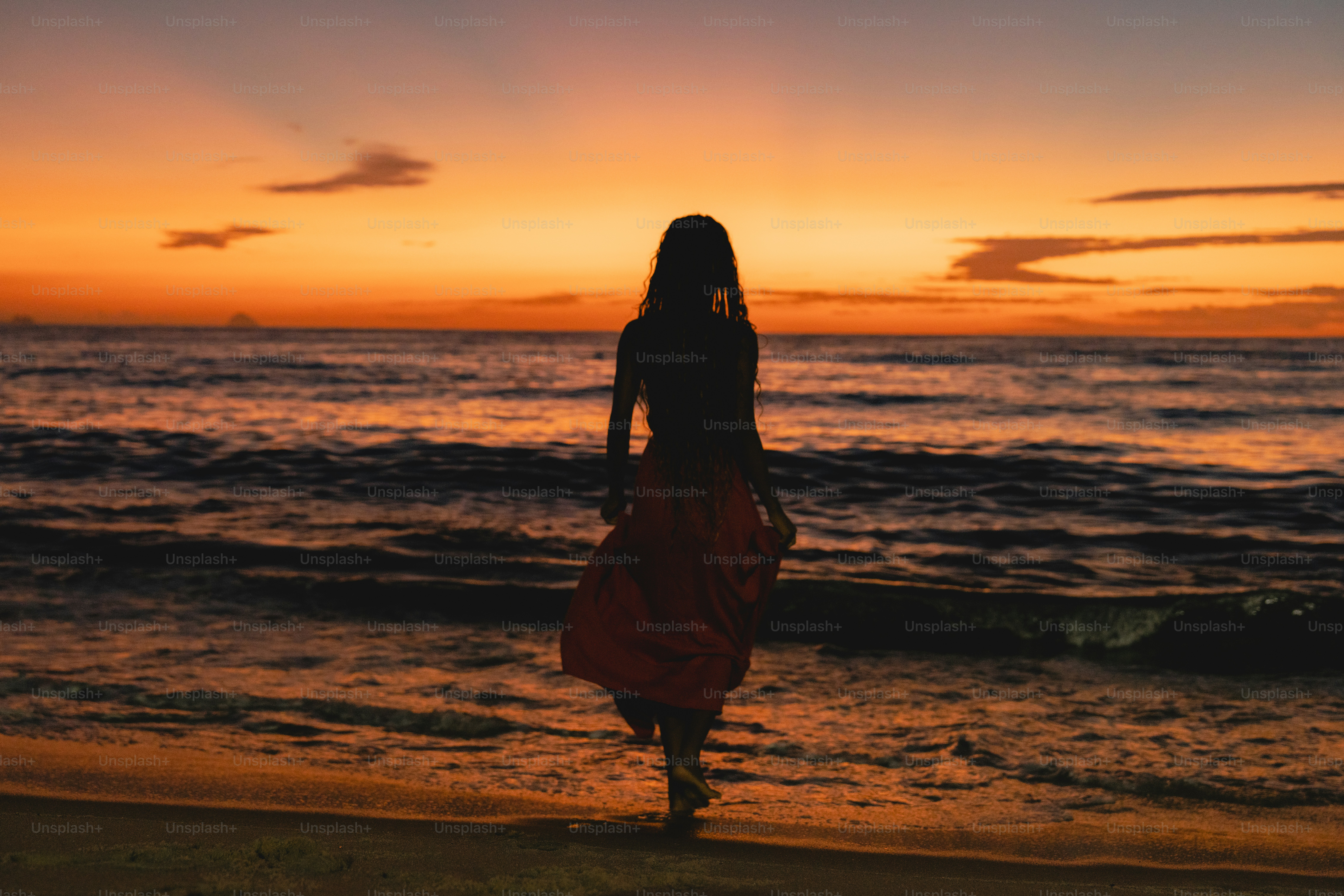 Uma mulher andando na praia ao pôr do sol