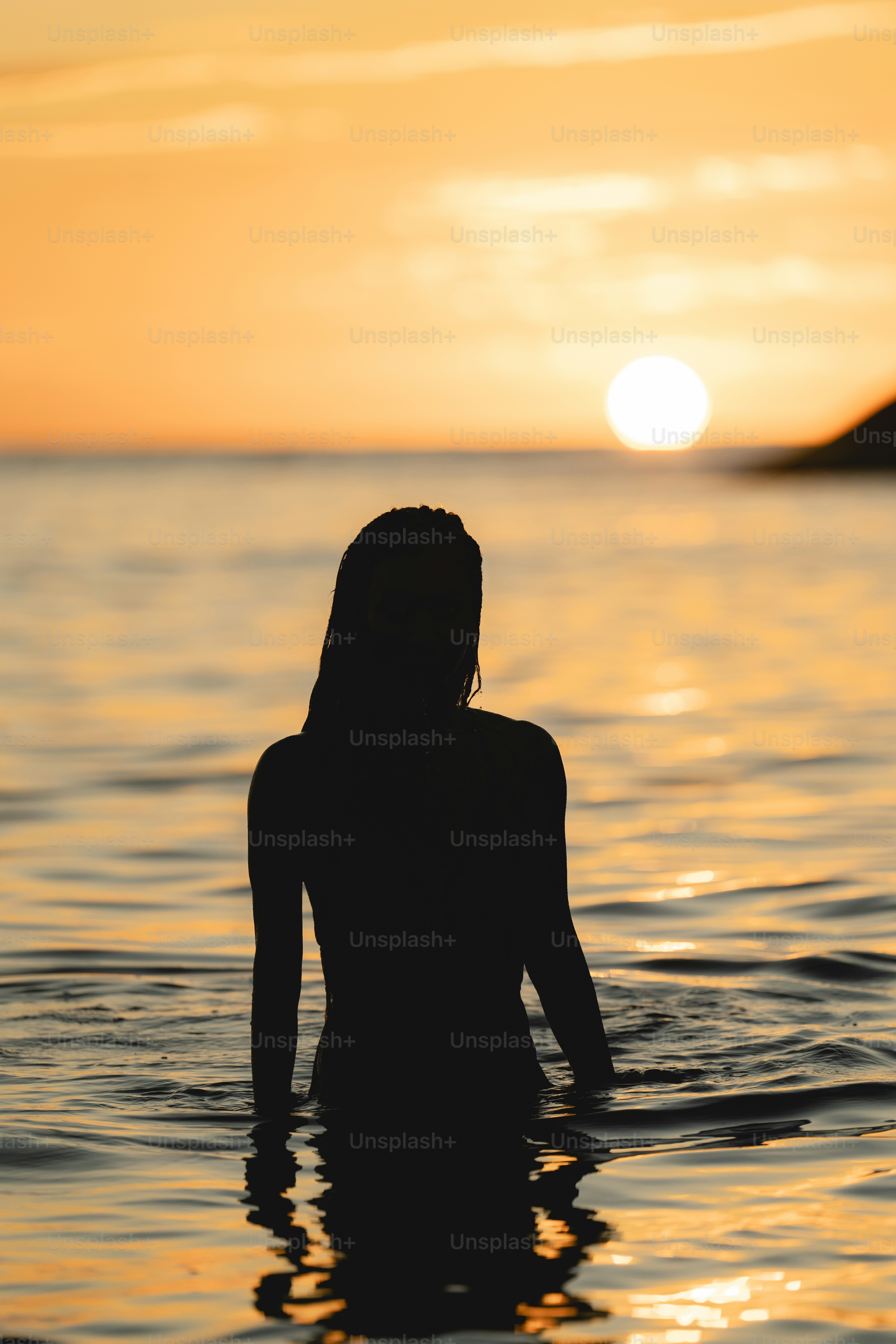 Uma mulher em pé na água ao pôr do sol