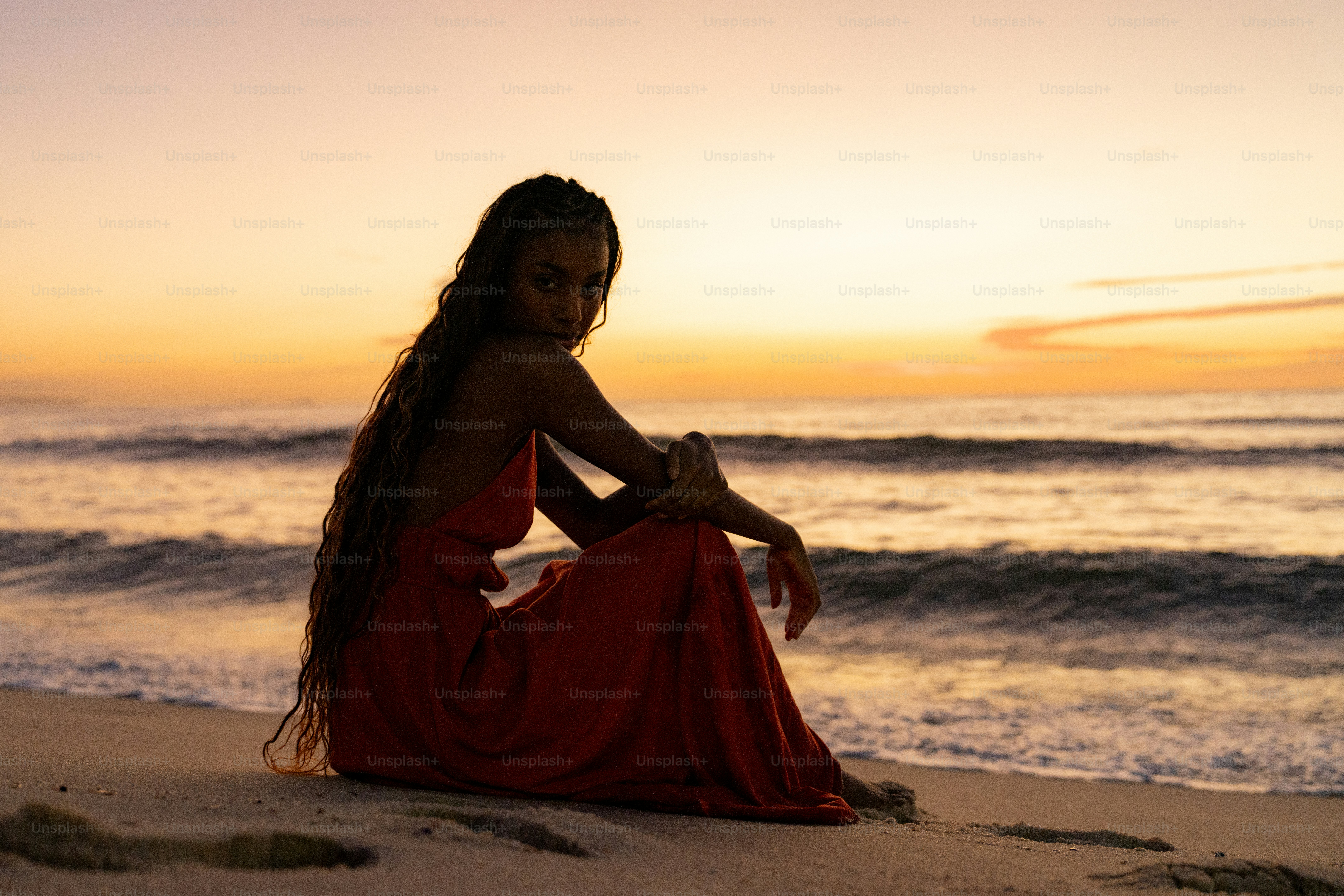 Uma mulher em um vestido vermelho que senta-se na praia