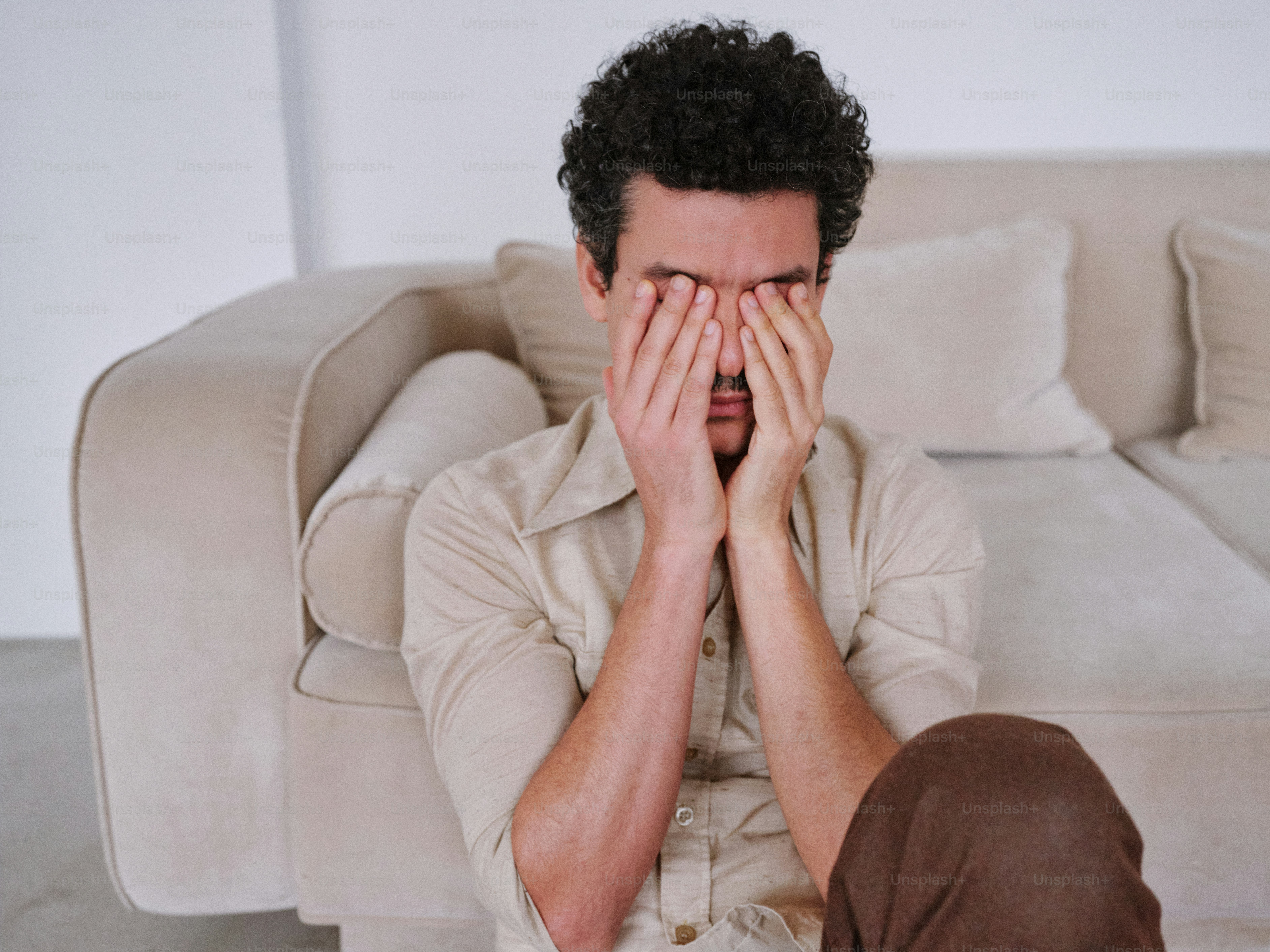 A man sitting on the floor covering his eyes