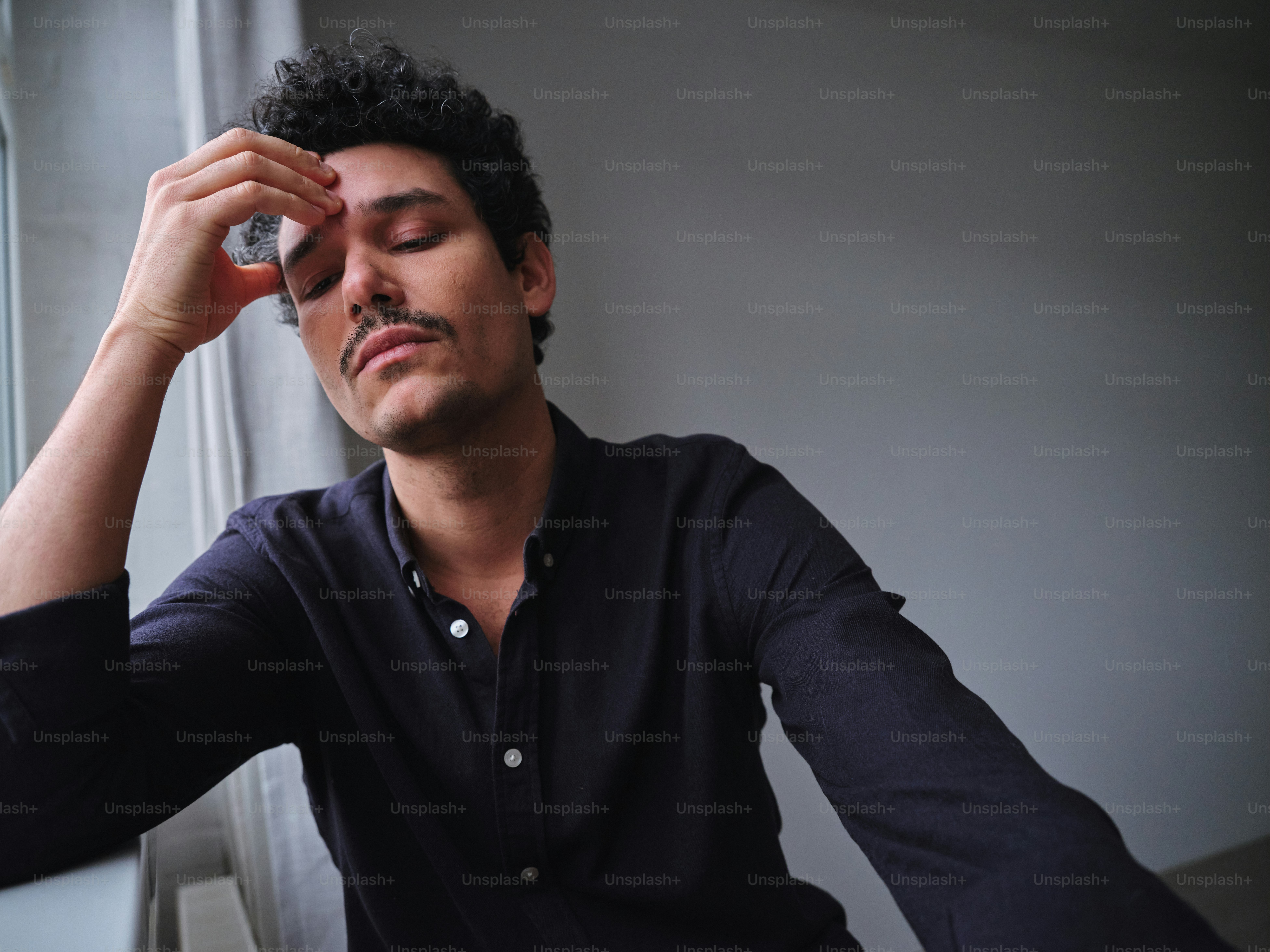 A man sitting in front of a window with his eyes closed