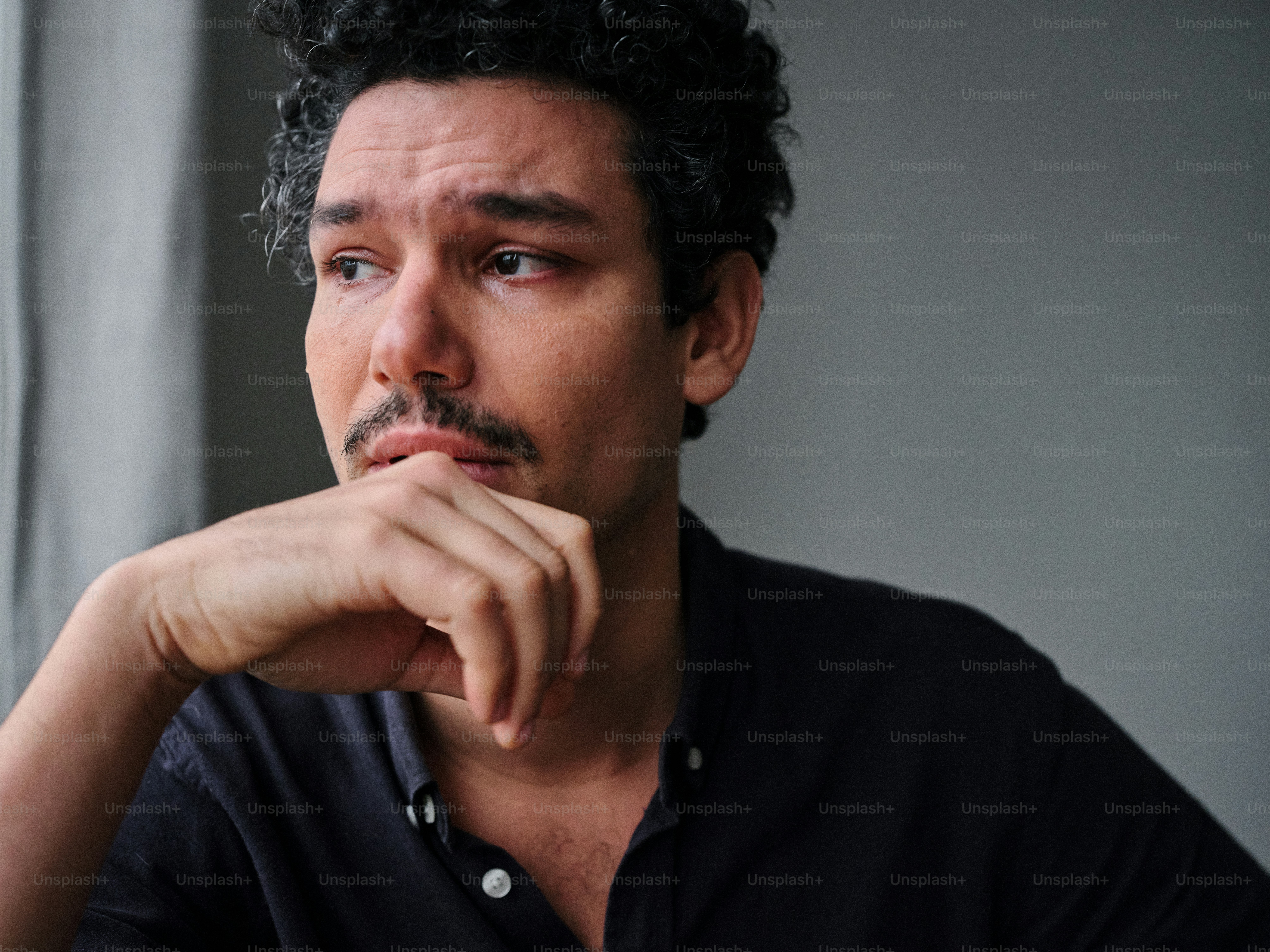 A man sitting in front of a window with his hand on his chin