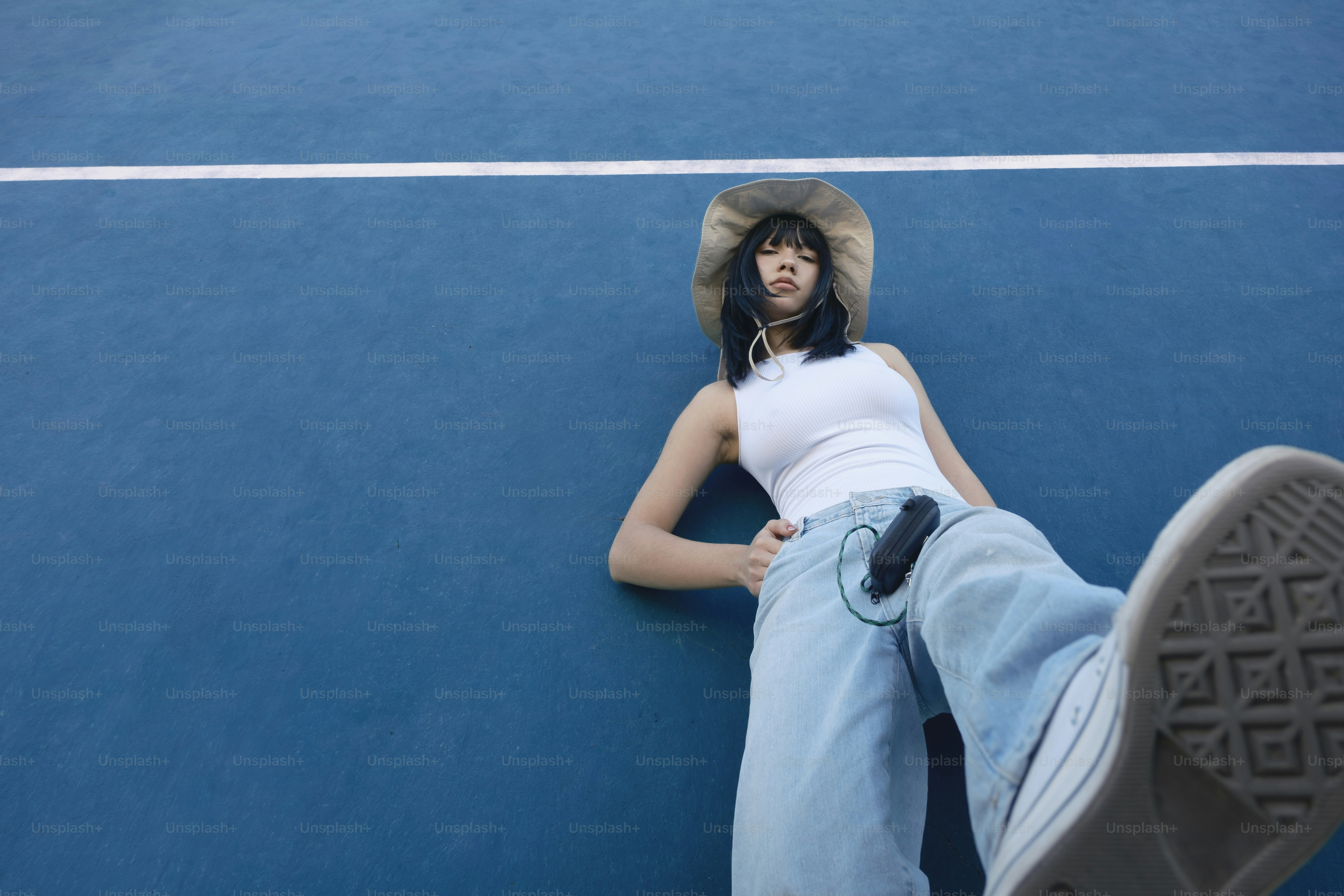 A person laying on a tennis court with a hat on