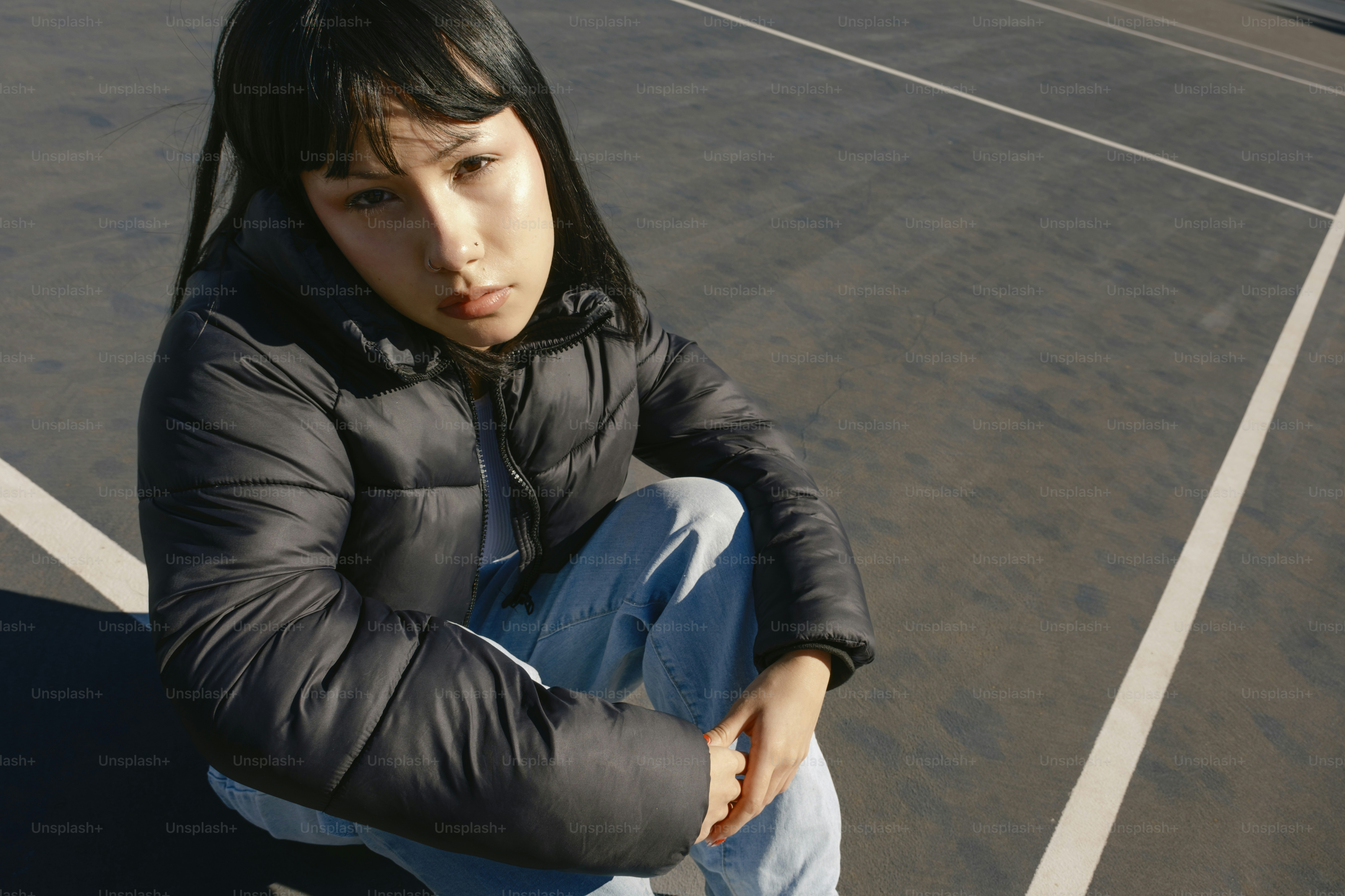 A young woman sitting on a skateboard in a parking lot