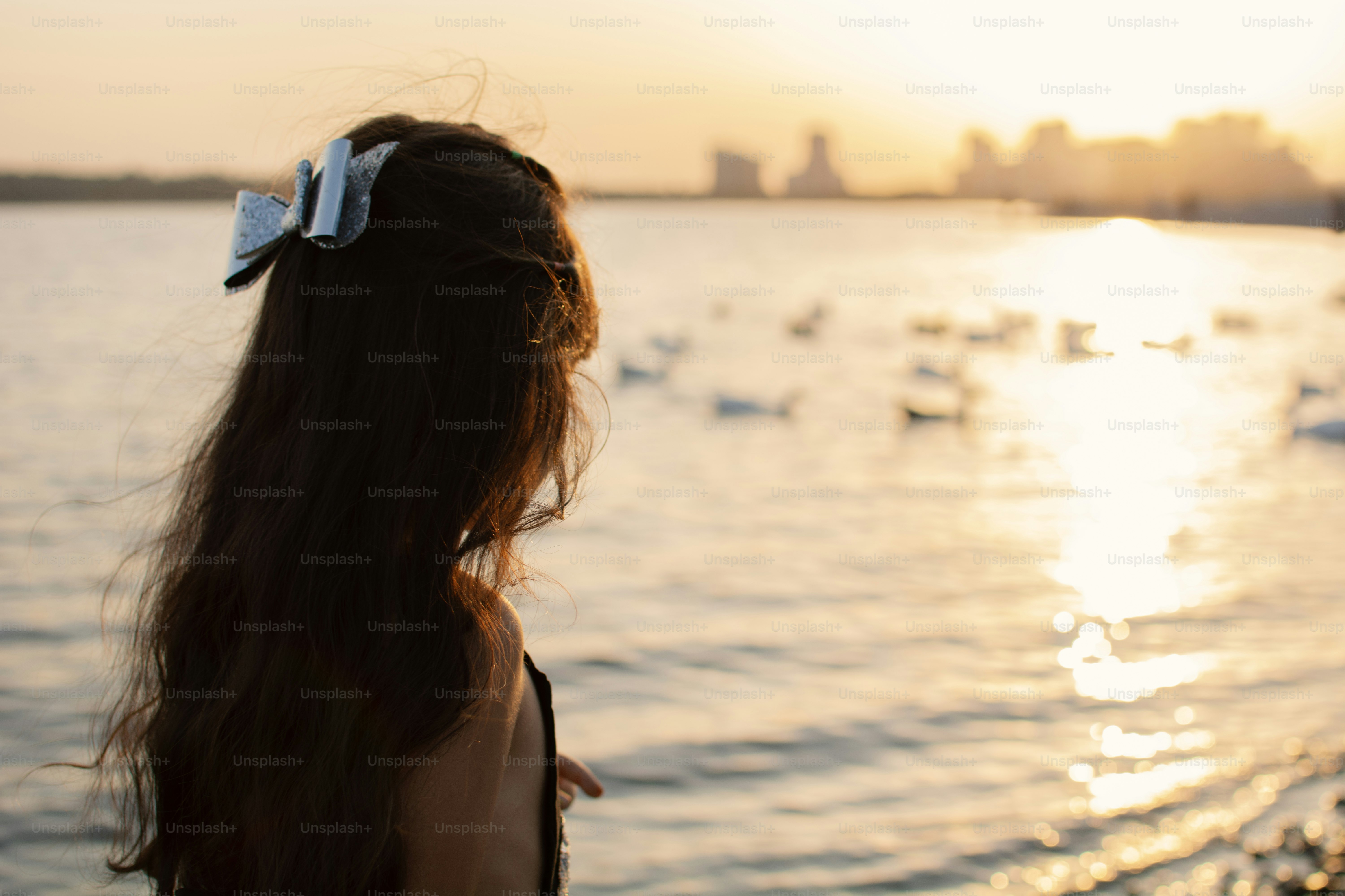 A woman standing on a beach next to a body of water photo – Golden hour ...
