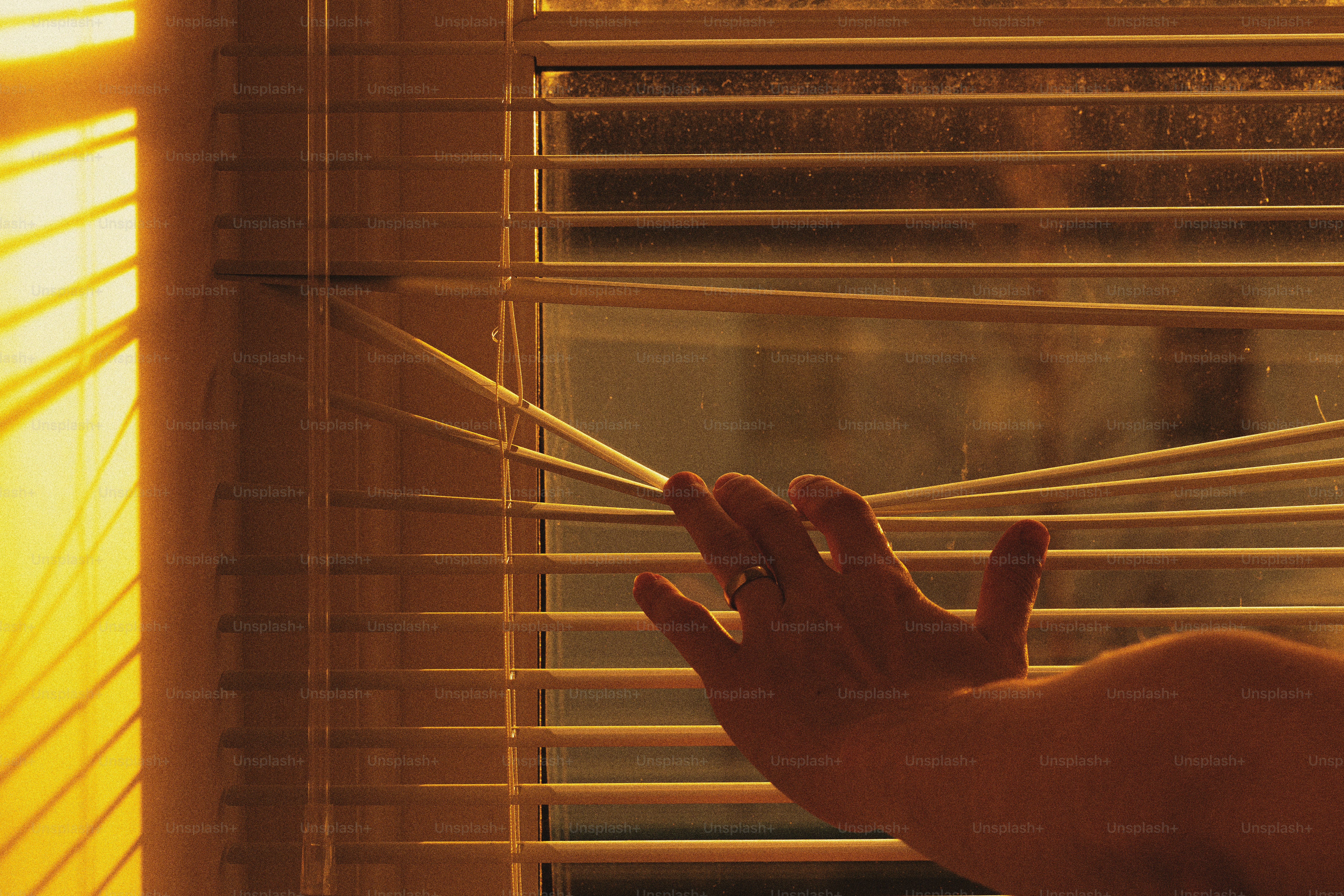 A person is looking out of a window with blinds