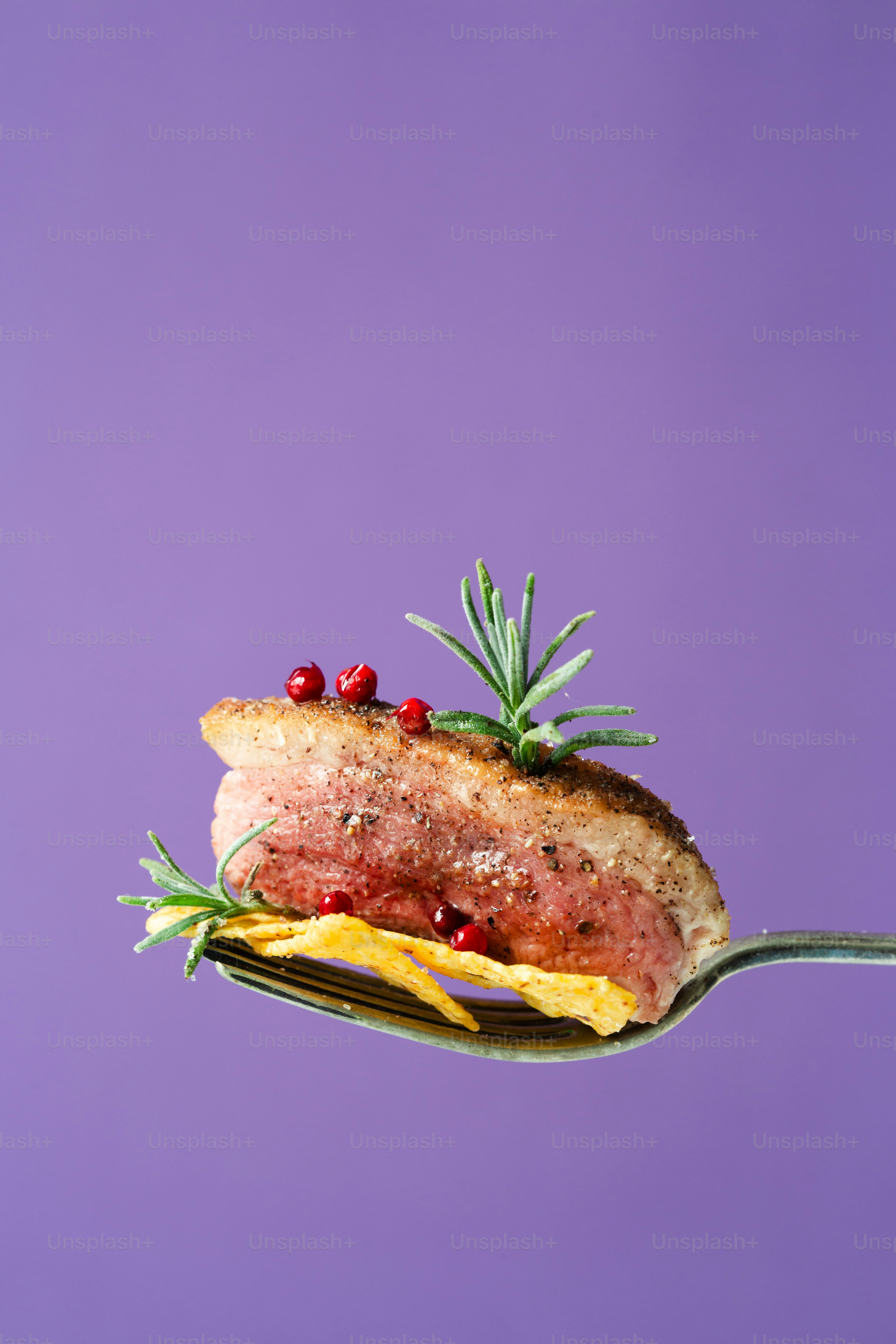 A piece of meat on a fork with a sprig of rosemary