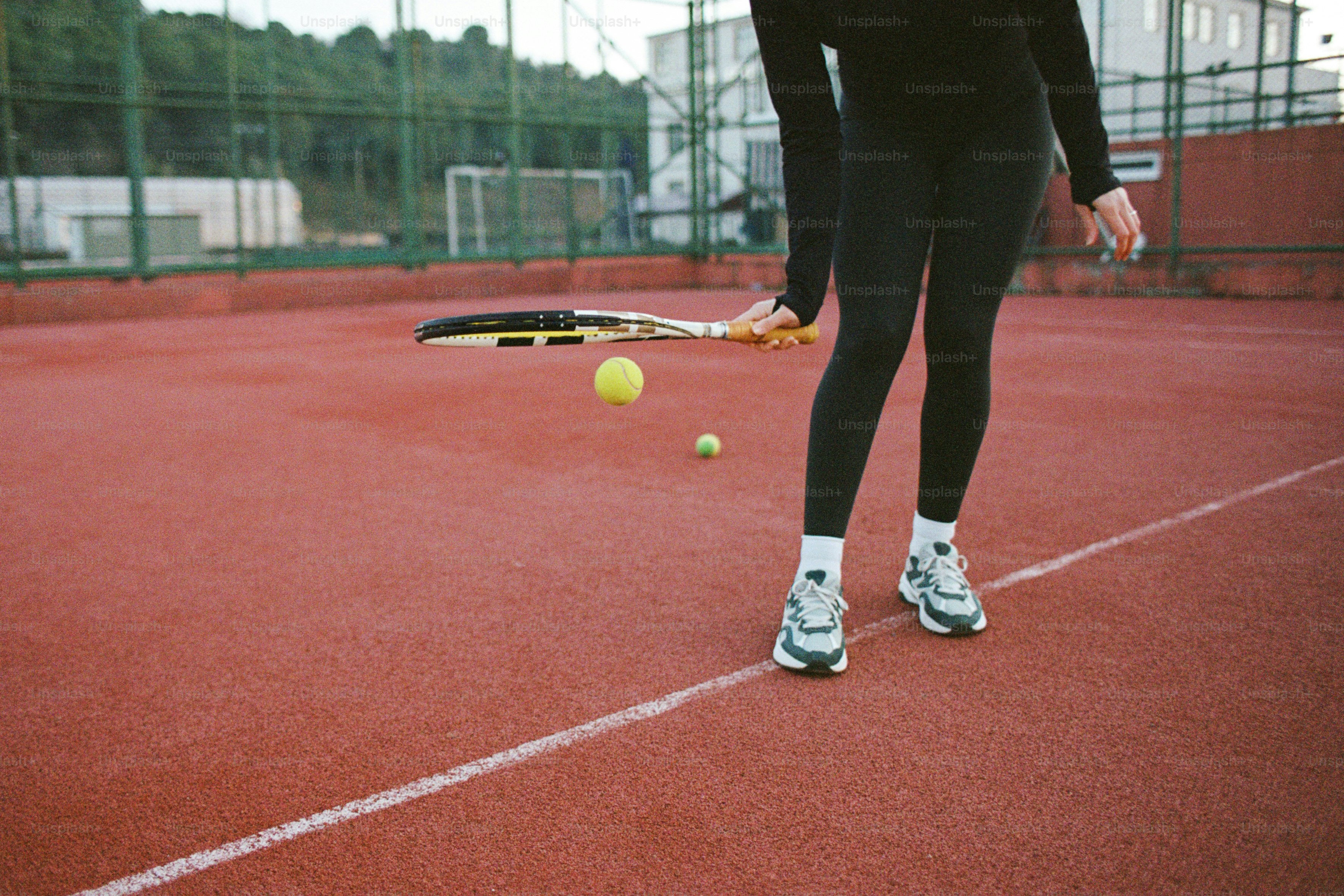 Seorang wanita berdiri di atas lapangan tenis sambil memegang raket