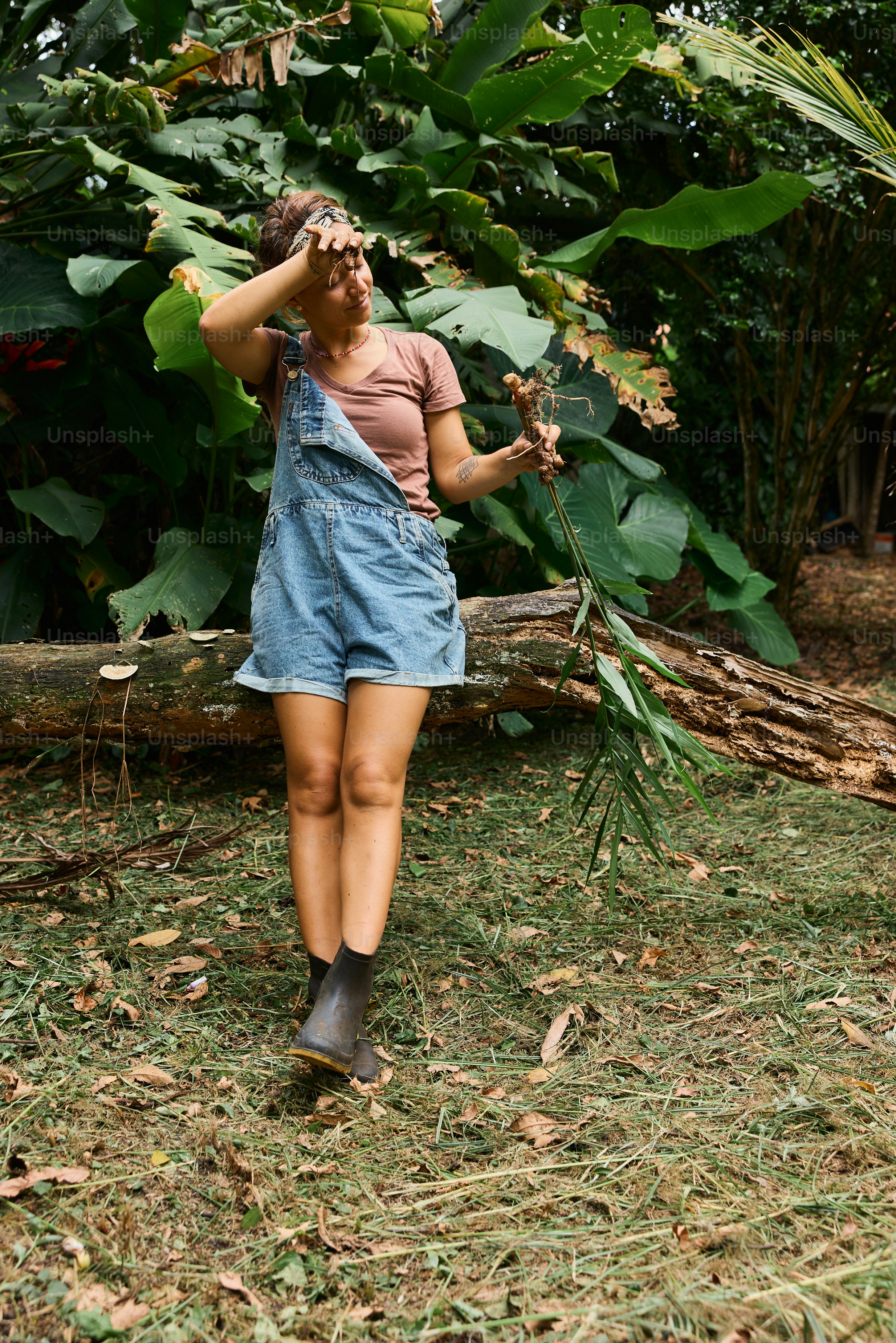 A woman in overalls is holding a plant