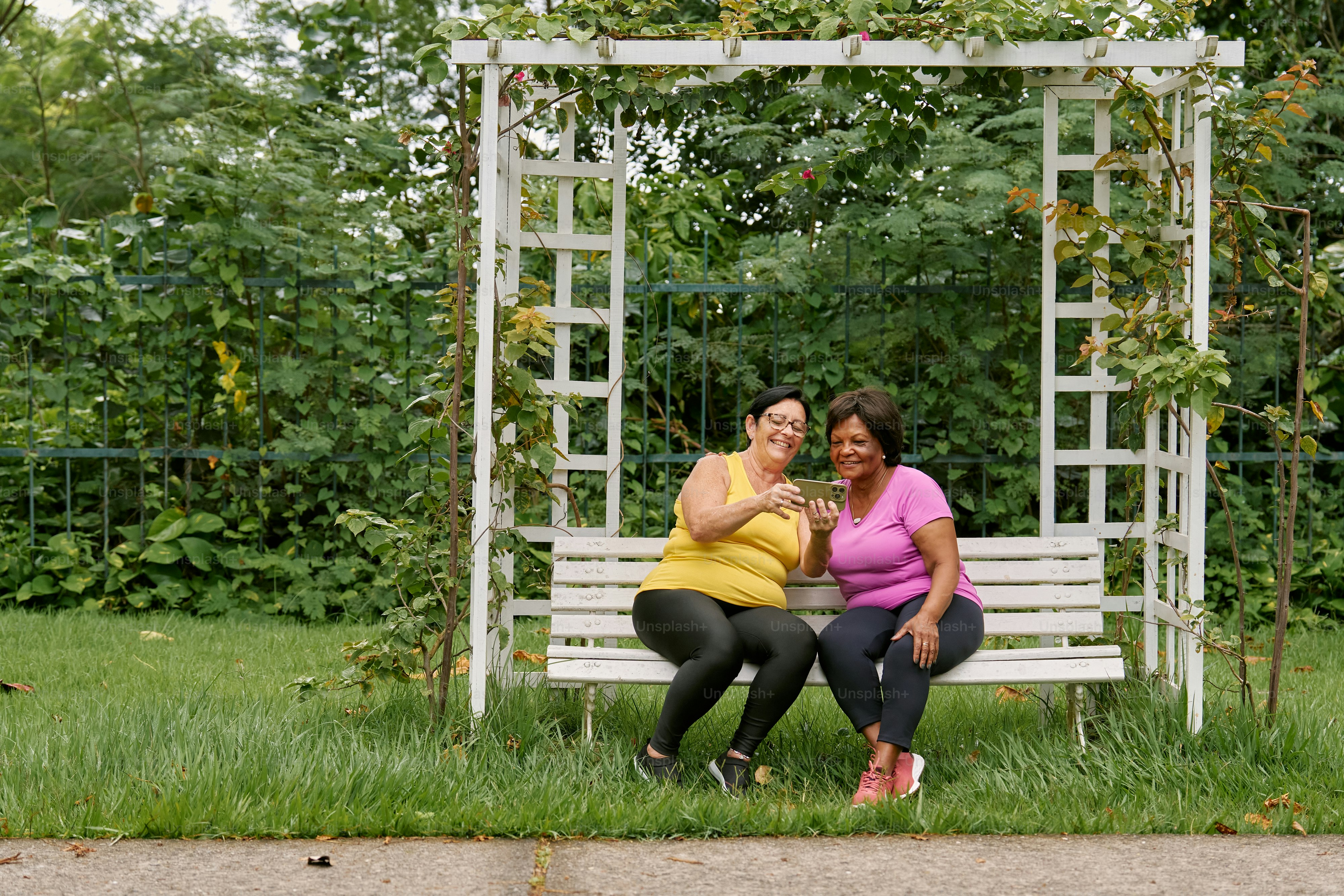A couple of women sitting on top of a white bench