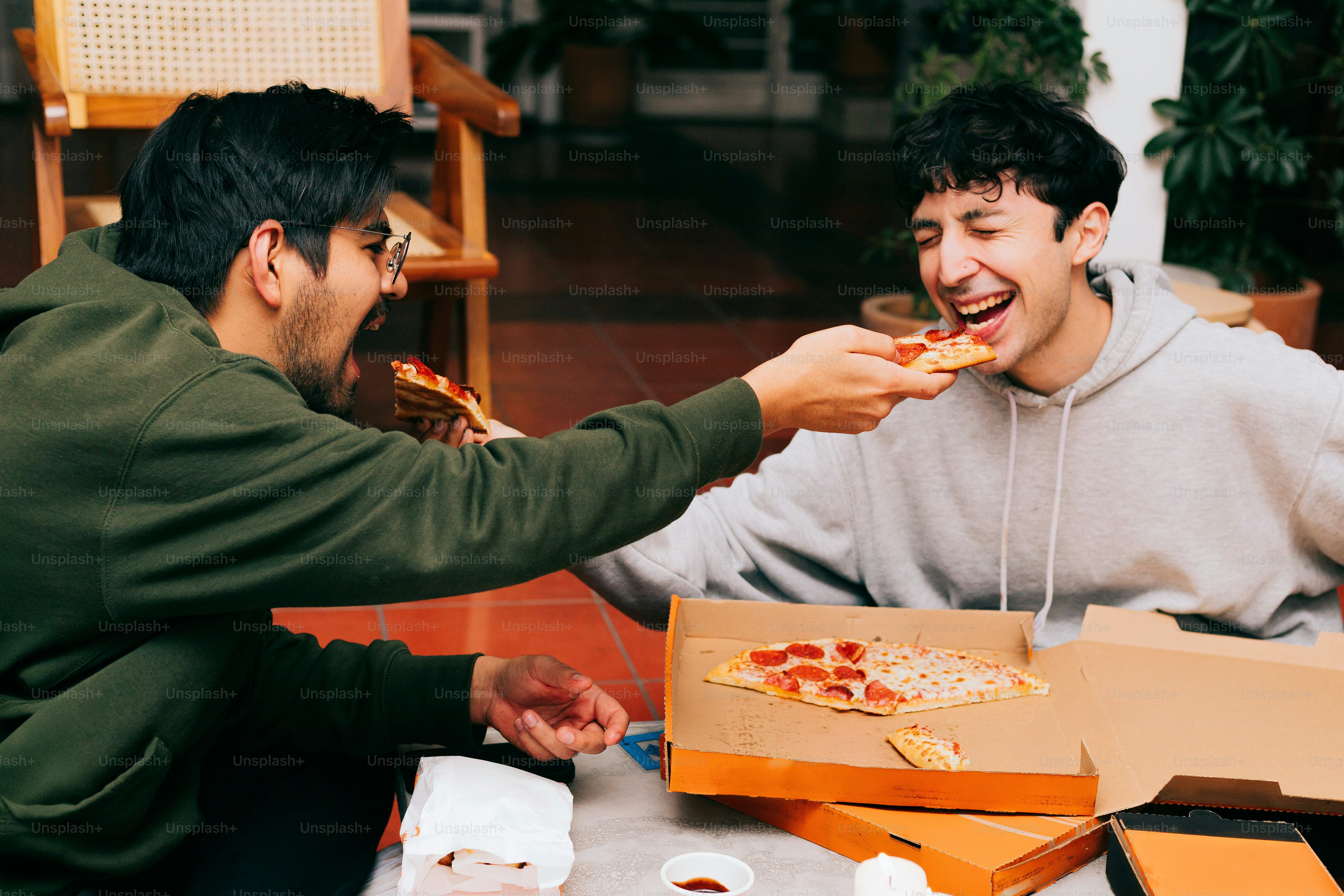 Two men are eating pizza at a table