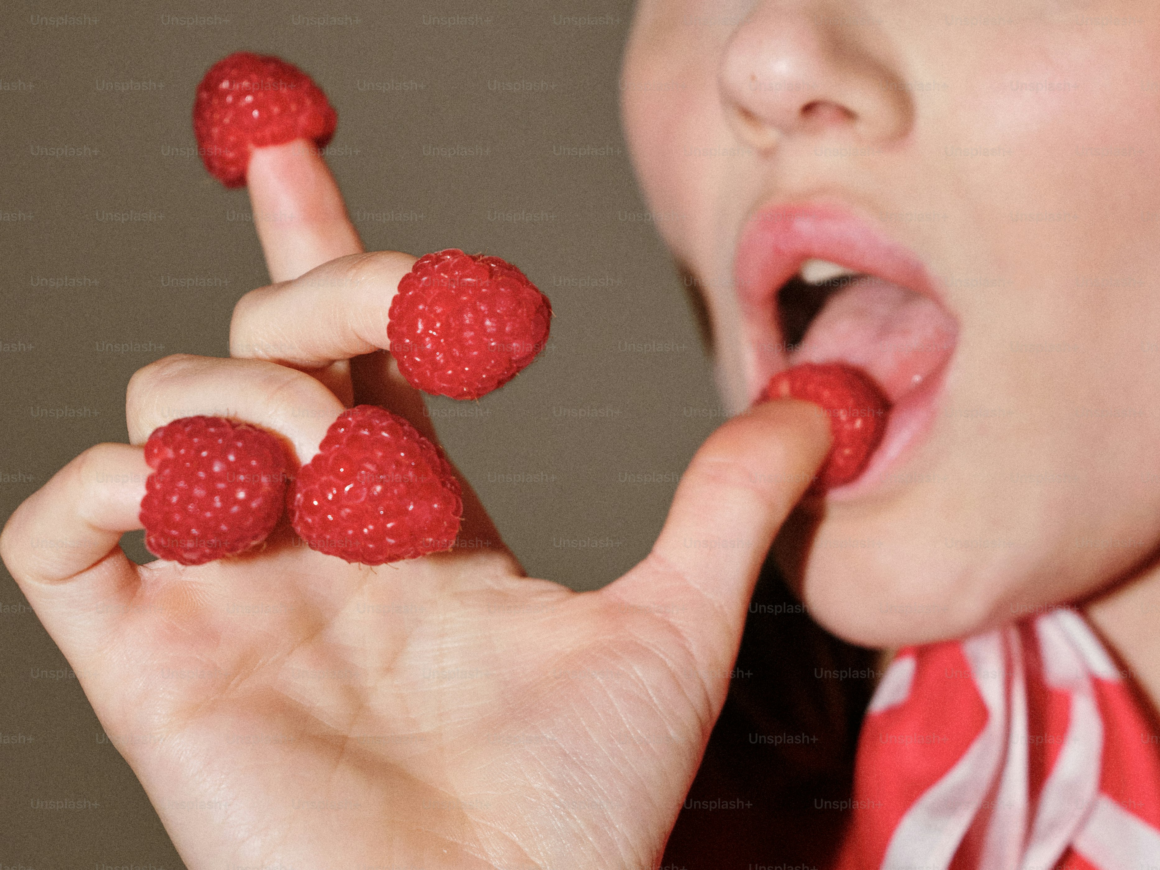A woman is holding raspberries in her mouth