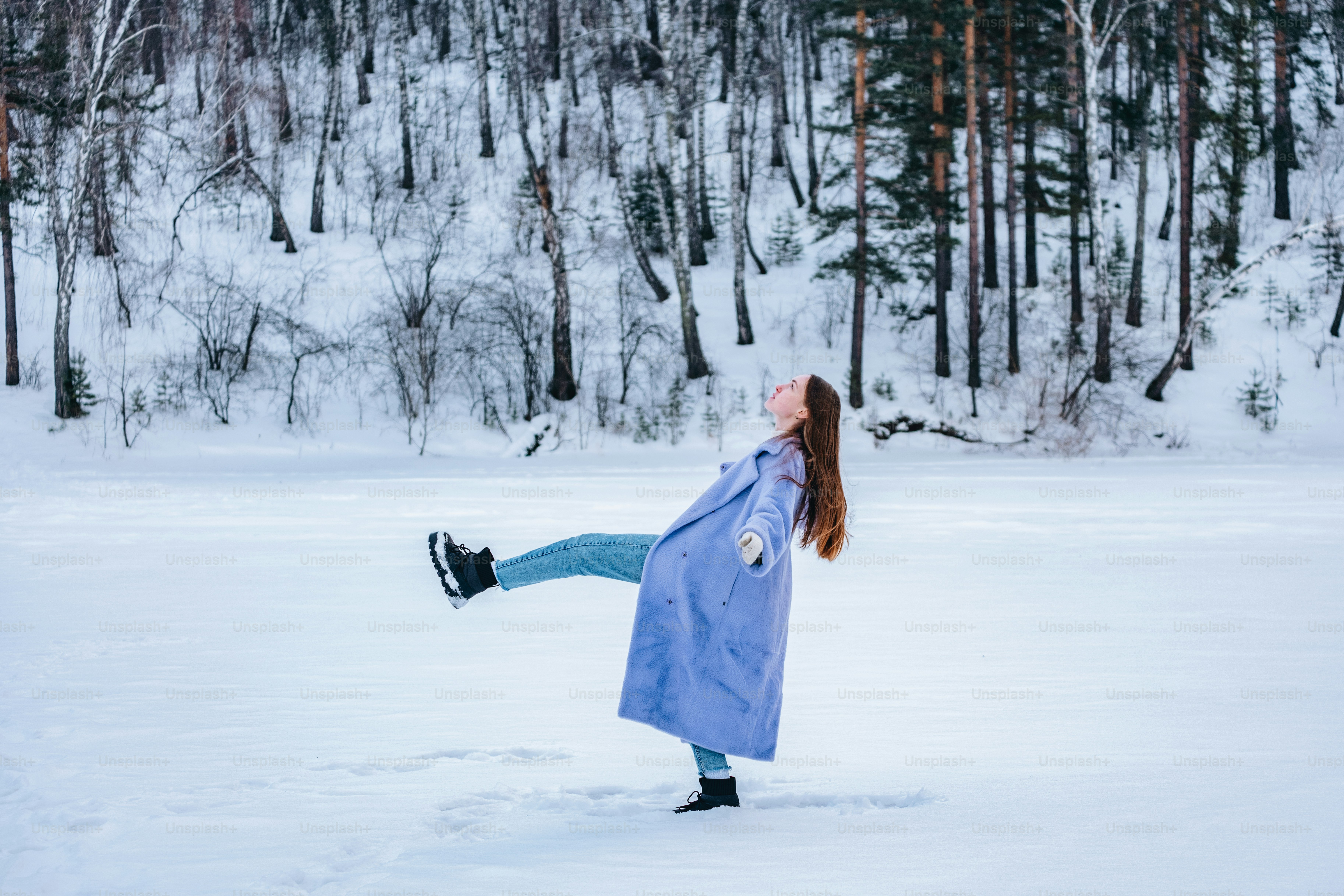 A woman in a blue coat is playing in the snow