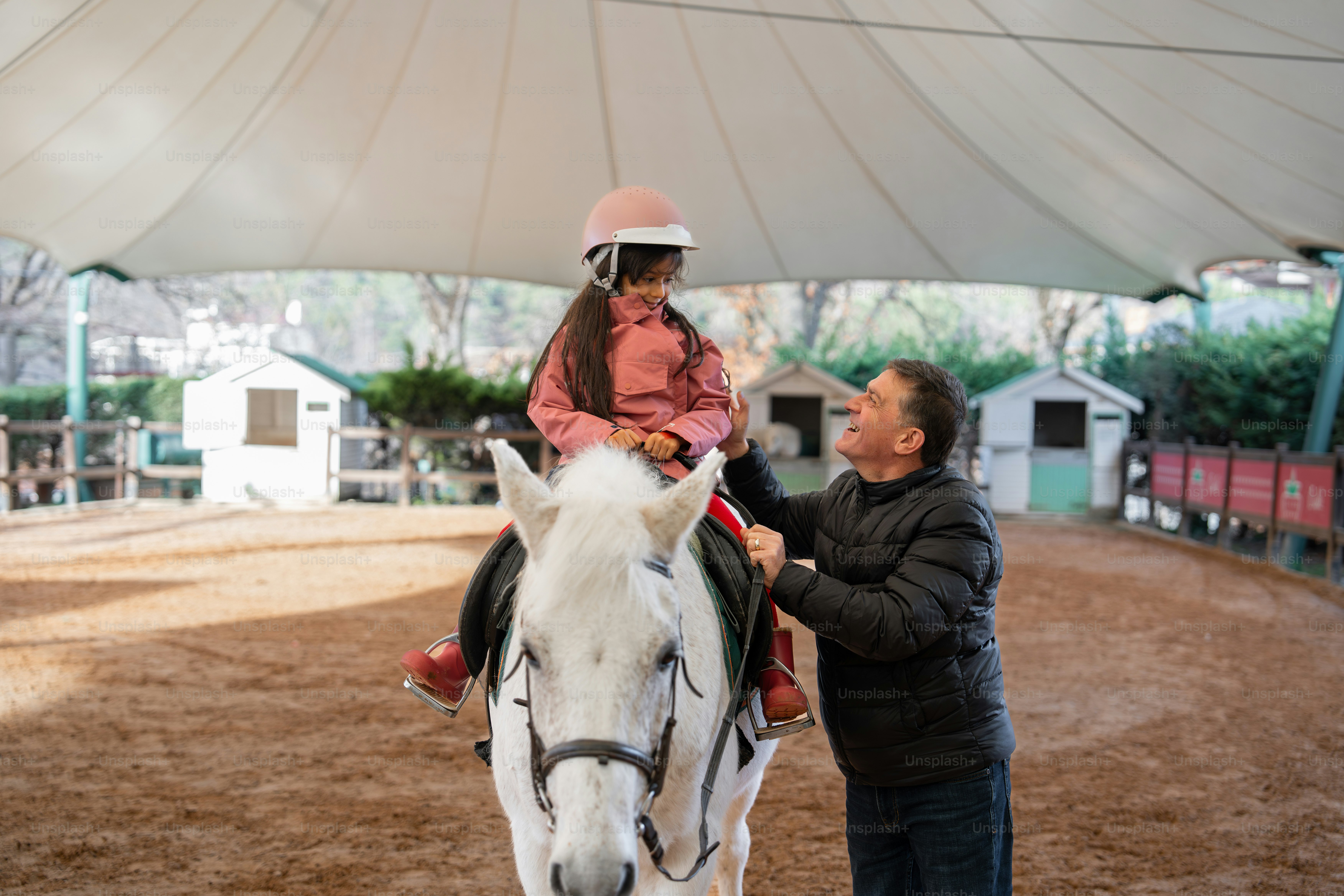A man and a little girl riding a horse under a tent