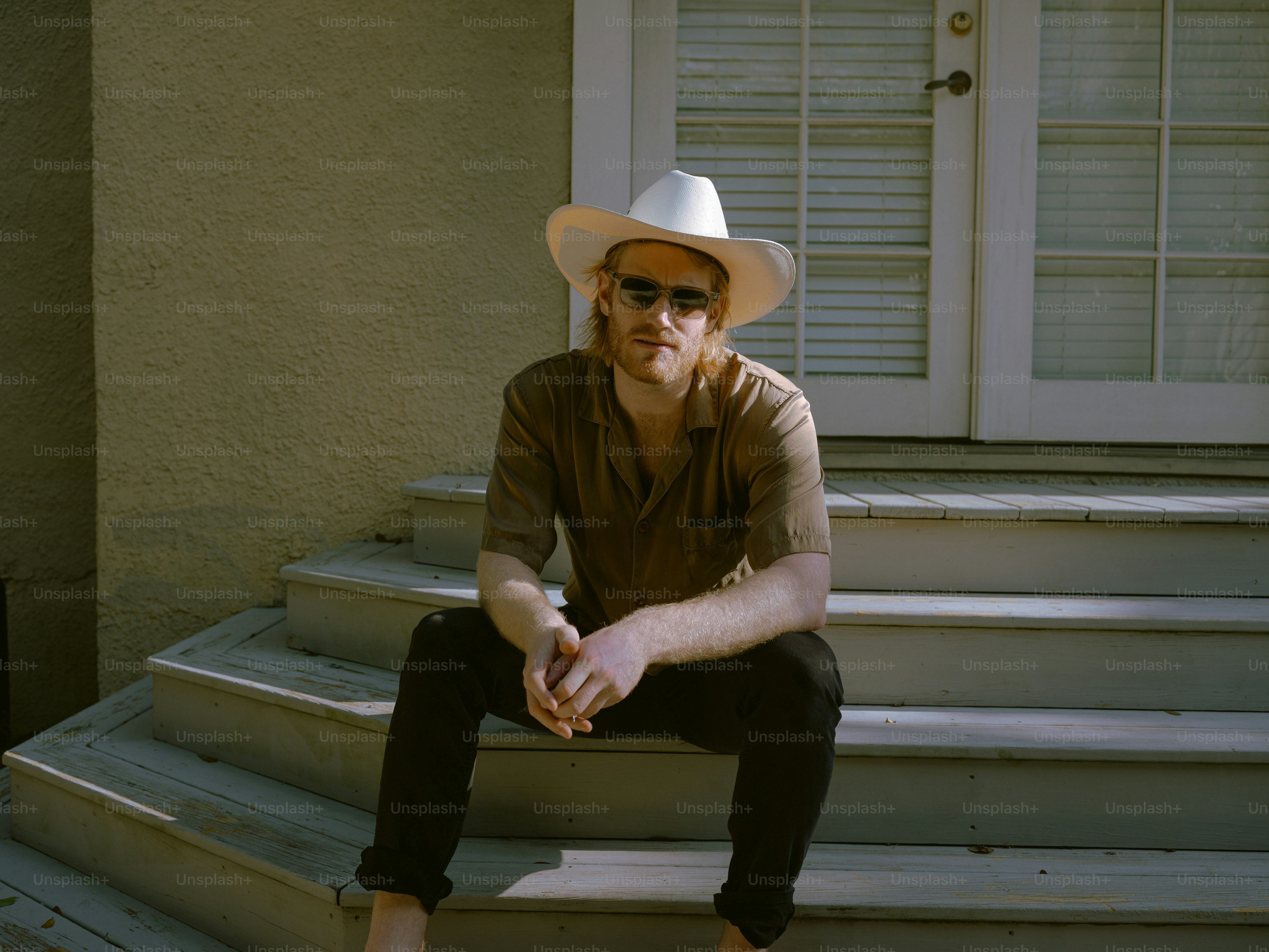 A man sitting on a step wearing a hat and sunglasses
